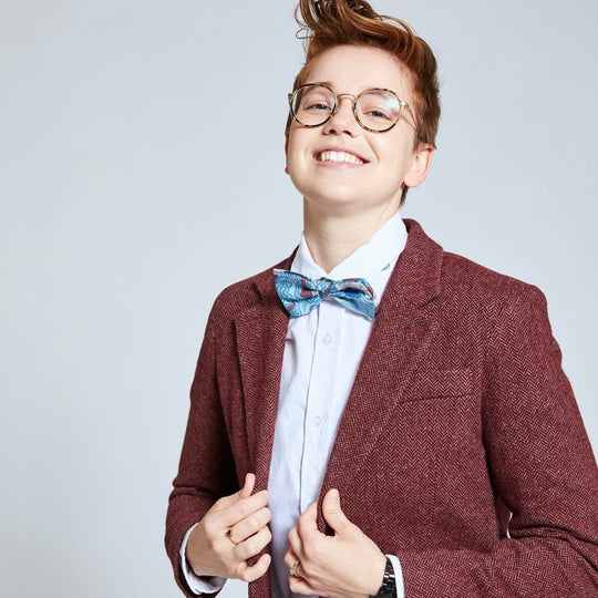 Androgynous model wearing Burgundy Tweed Blazer with White shirt and geographic bow tie. Hands lightly clasping blazer lapels