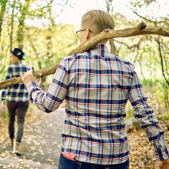 An androgynous model shot from behind wearing brushed flannel outdoors while holding a big stick