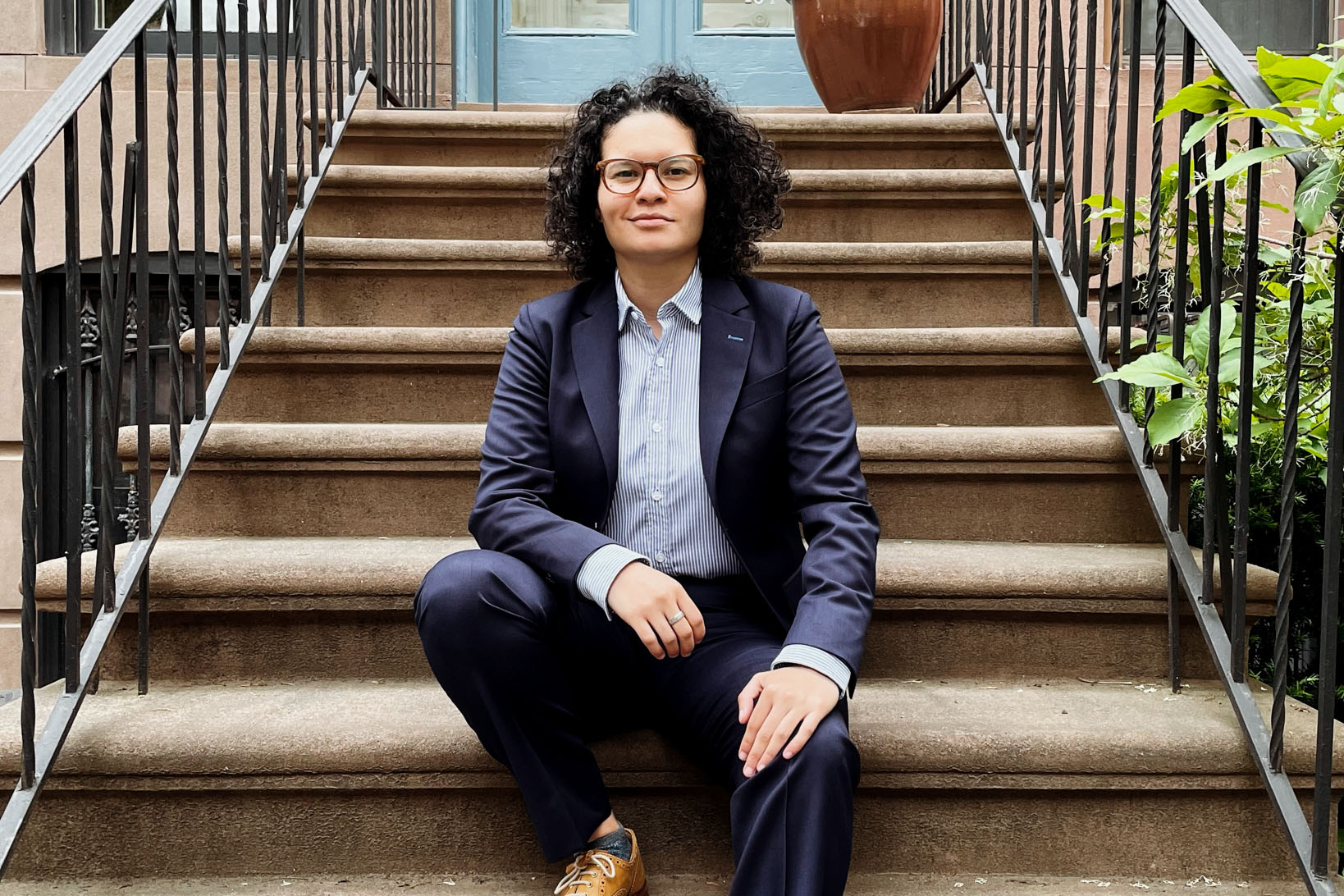 Amanda Urrego in a suit sitting on a stoop.
