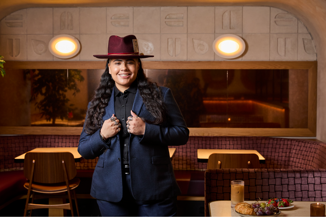 Model wearing a navy hopsack suit and burgundy hat in a restaurant.