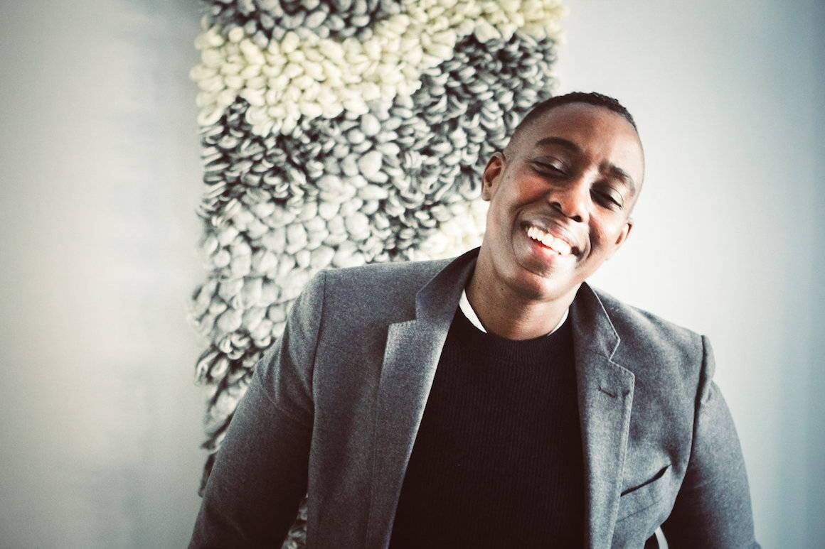 Smiling person in a gray blazer and black top, an androgynous professional style look for the office