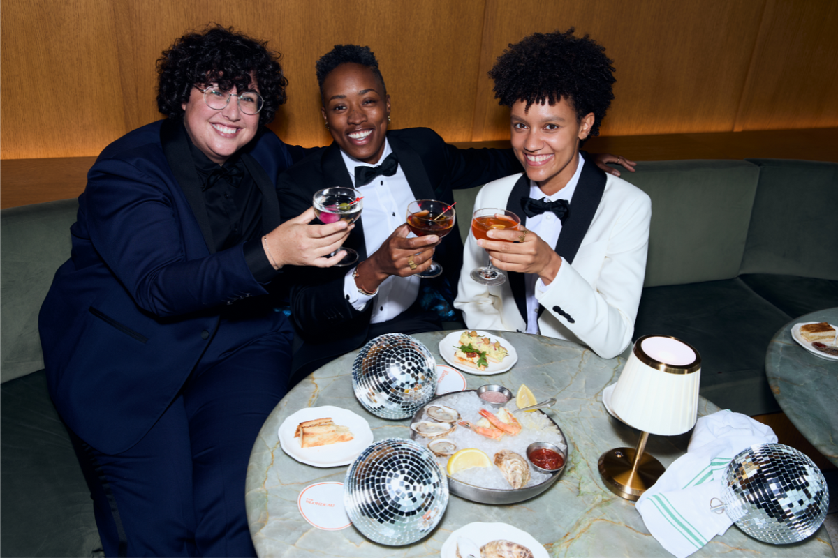 Three people in formal attire sitting around a table with food and drinks, including disco balls.