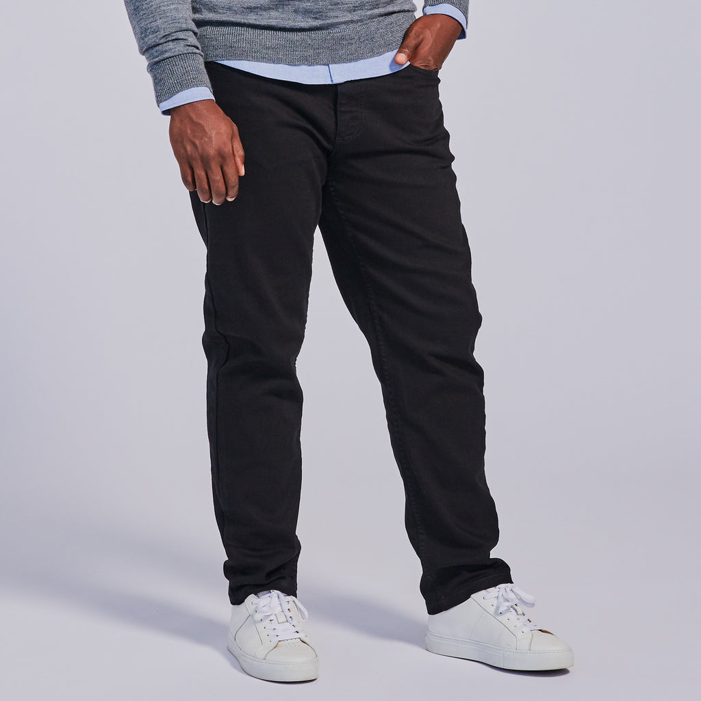 A person standing against a plain background, wearing slim-tapered black jeans and white sneakers.