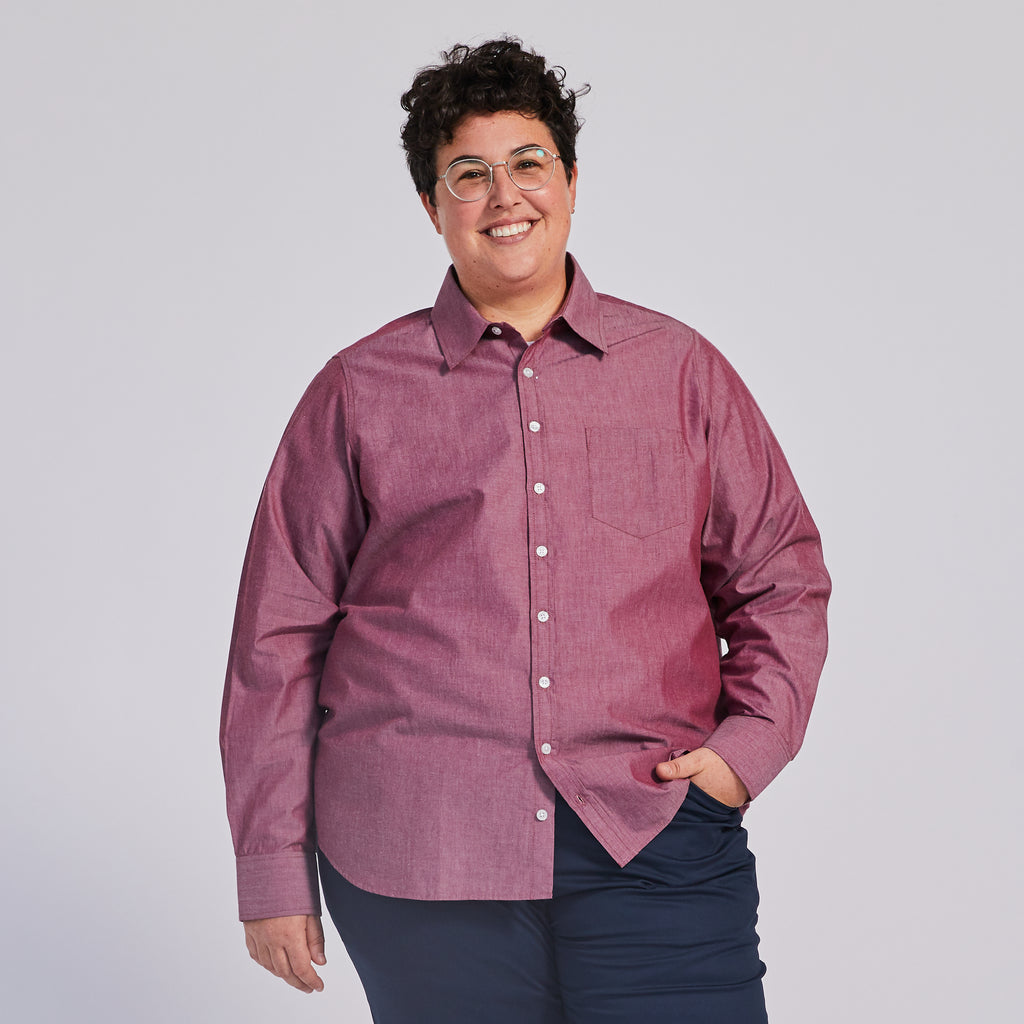 A person smiling and wearing a red chambray point collar shirt with buttons down the front.