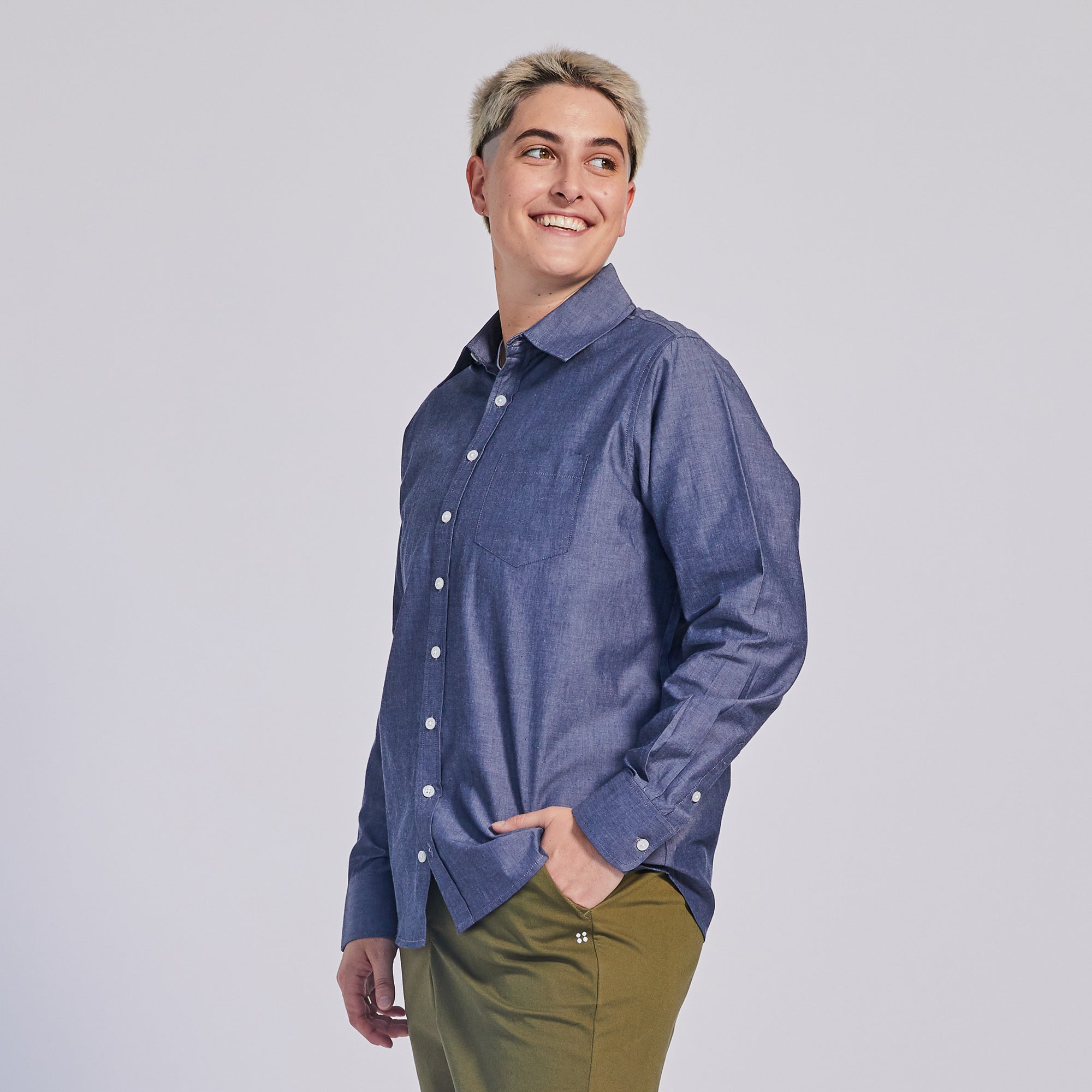 Model wearing a blue chambray long-sleeve shirt smiling with their hand in their  pocket. . Color: Blue Chambray