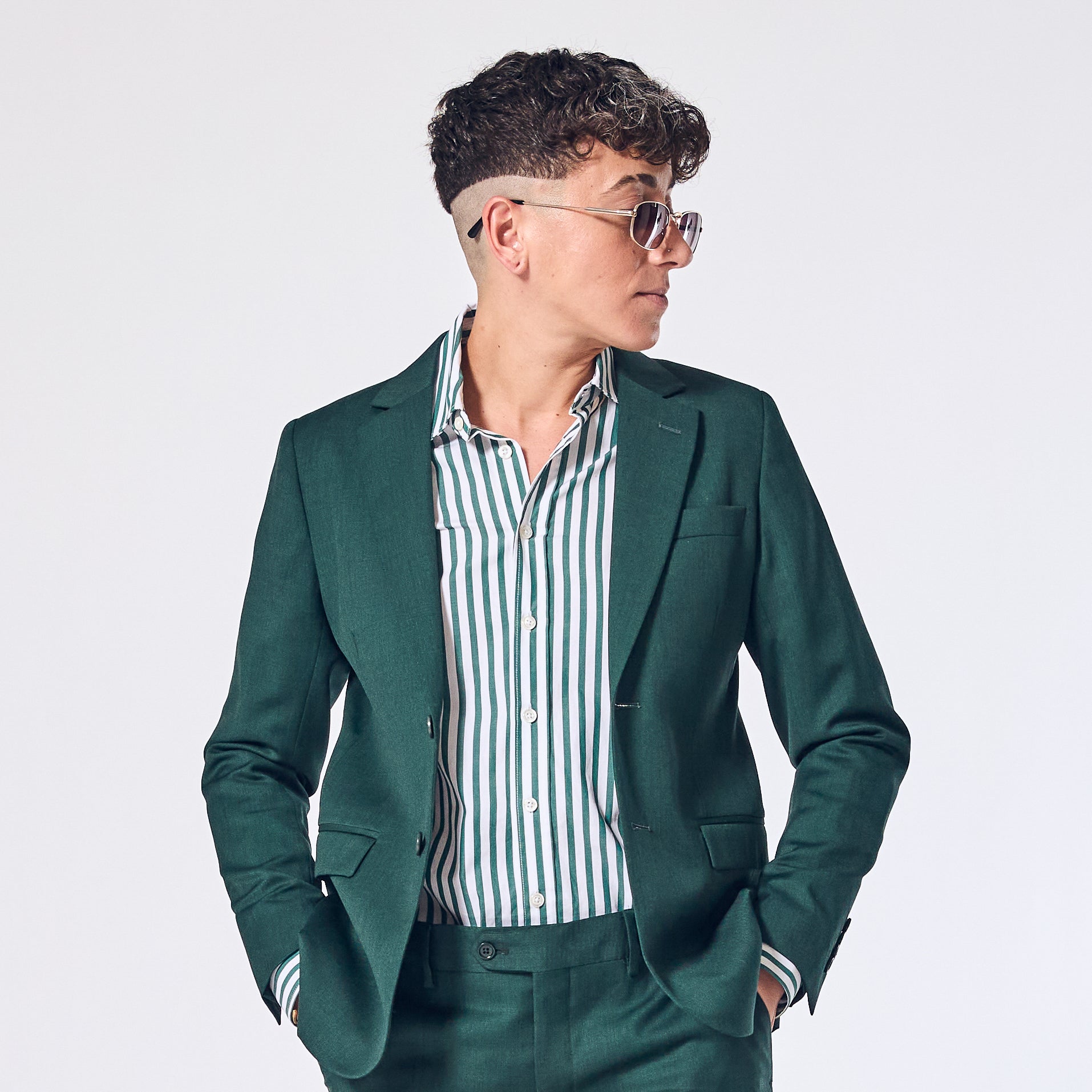 androgynous person wearing a green blazer over a striped shirt on a white background