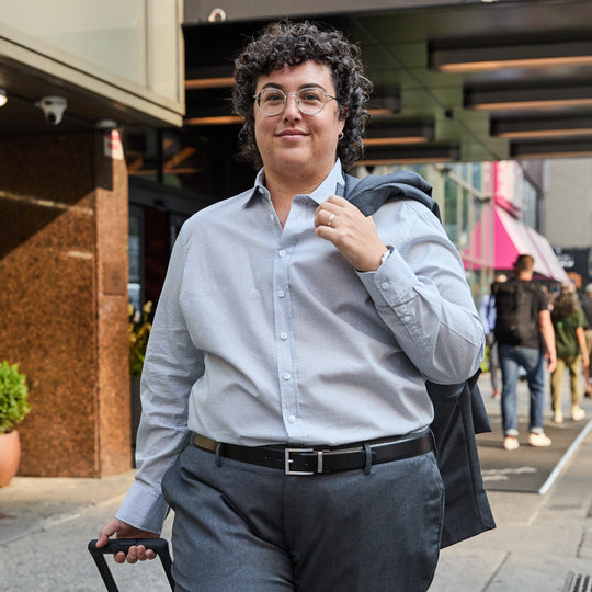 Person in a light blue shirt and dark pants standing on a city street.