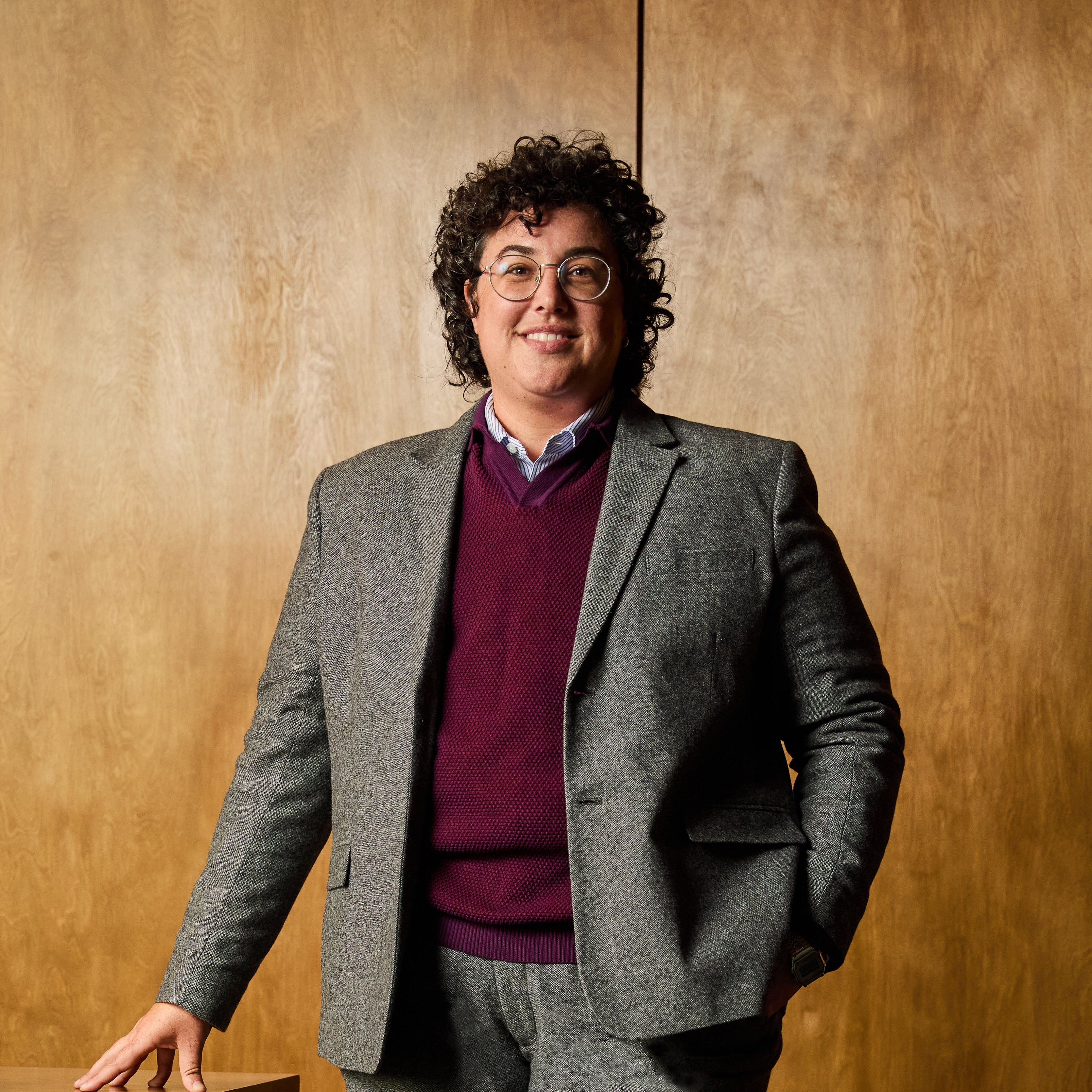 Person wearing a gray blazer and purple sweater against a wooden background
