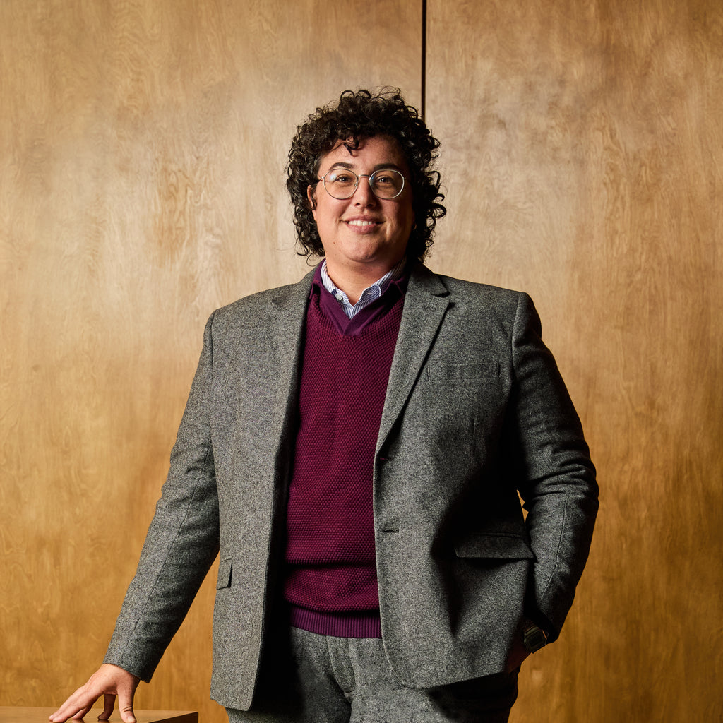 Person wearing a gray blazer and purple sweater against a wooden background