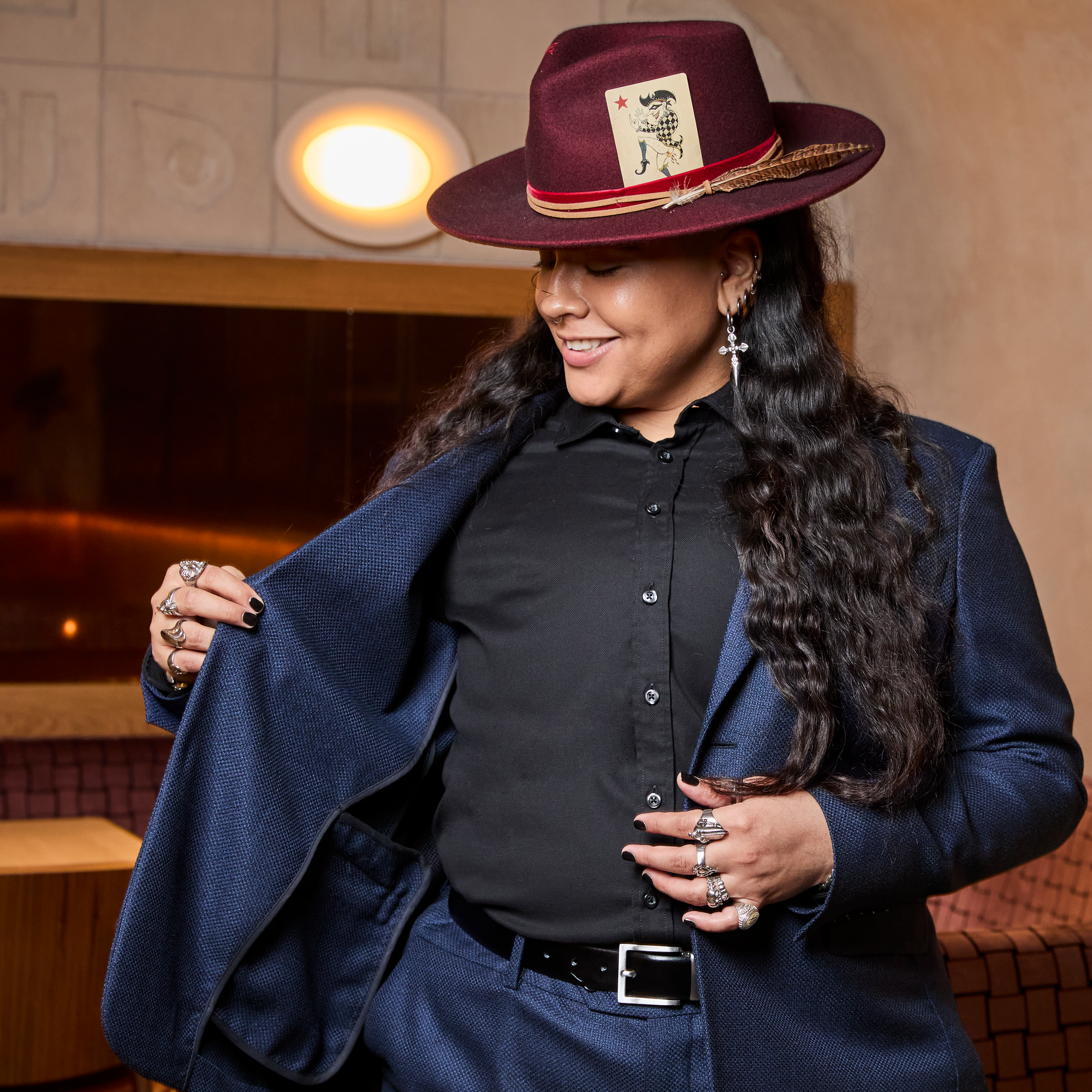 Model wearing a textured navy blazer, black shirt, and maroon hat with decorative elements. Color: Navy Textured