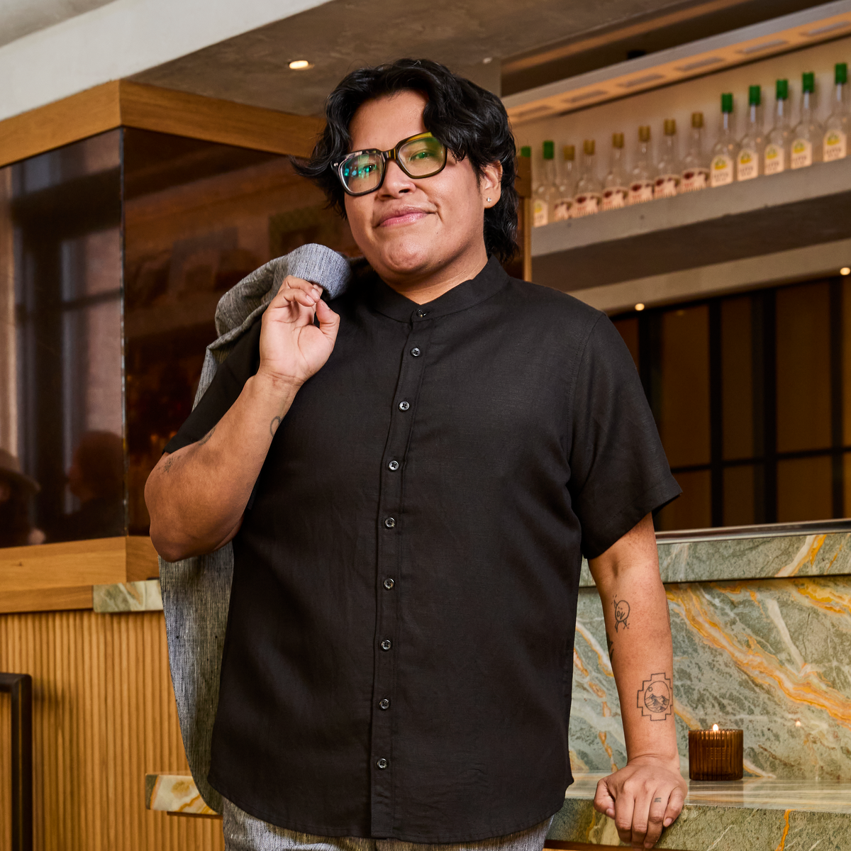 Model wearing a black shirt and glasses in a bar setting. Color: Black