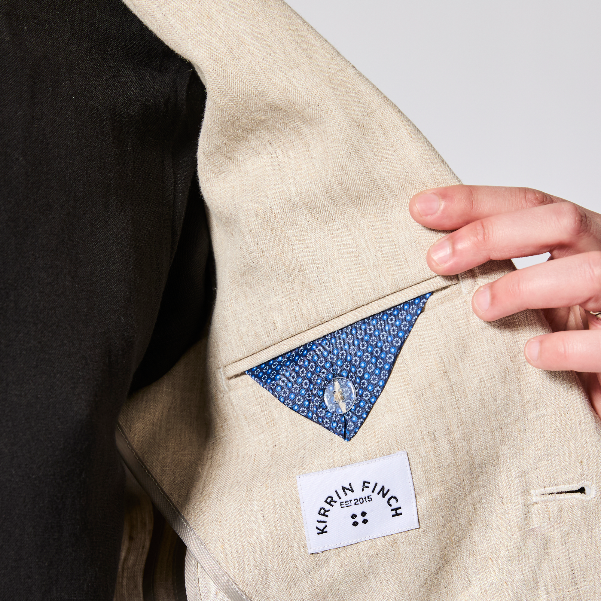 Beige jacket with a hand opening a pocket revealing a blue patterned lining, with 'Kirrin Finch' label. Color: Khaki Herringbone