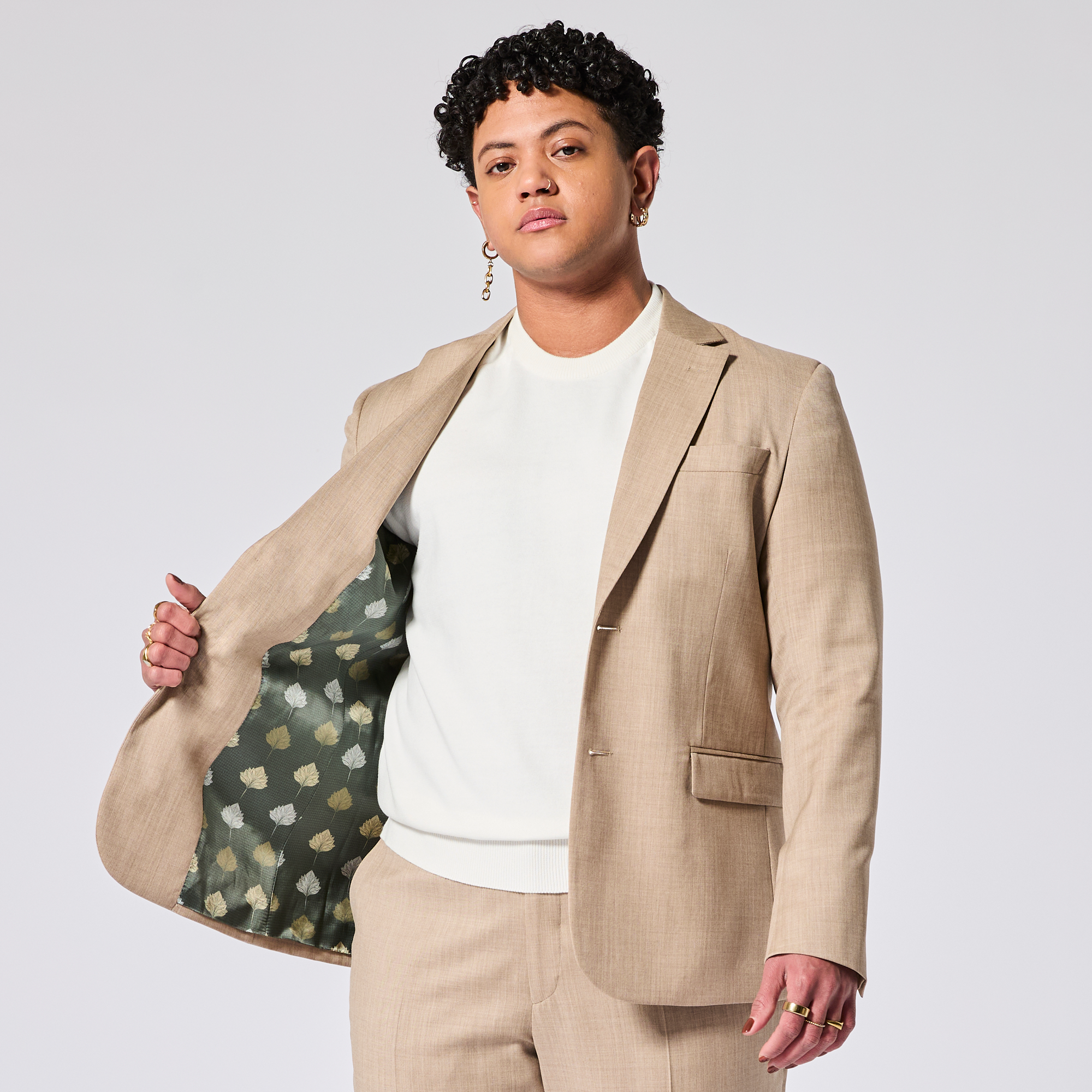 A person wearing a beige suit with a white shirt and showing the patterned lining. Color: Desert