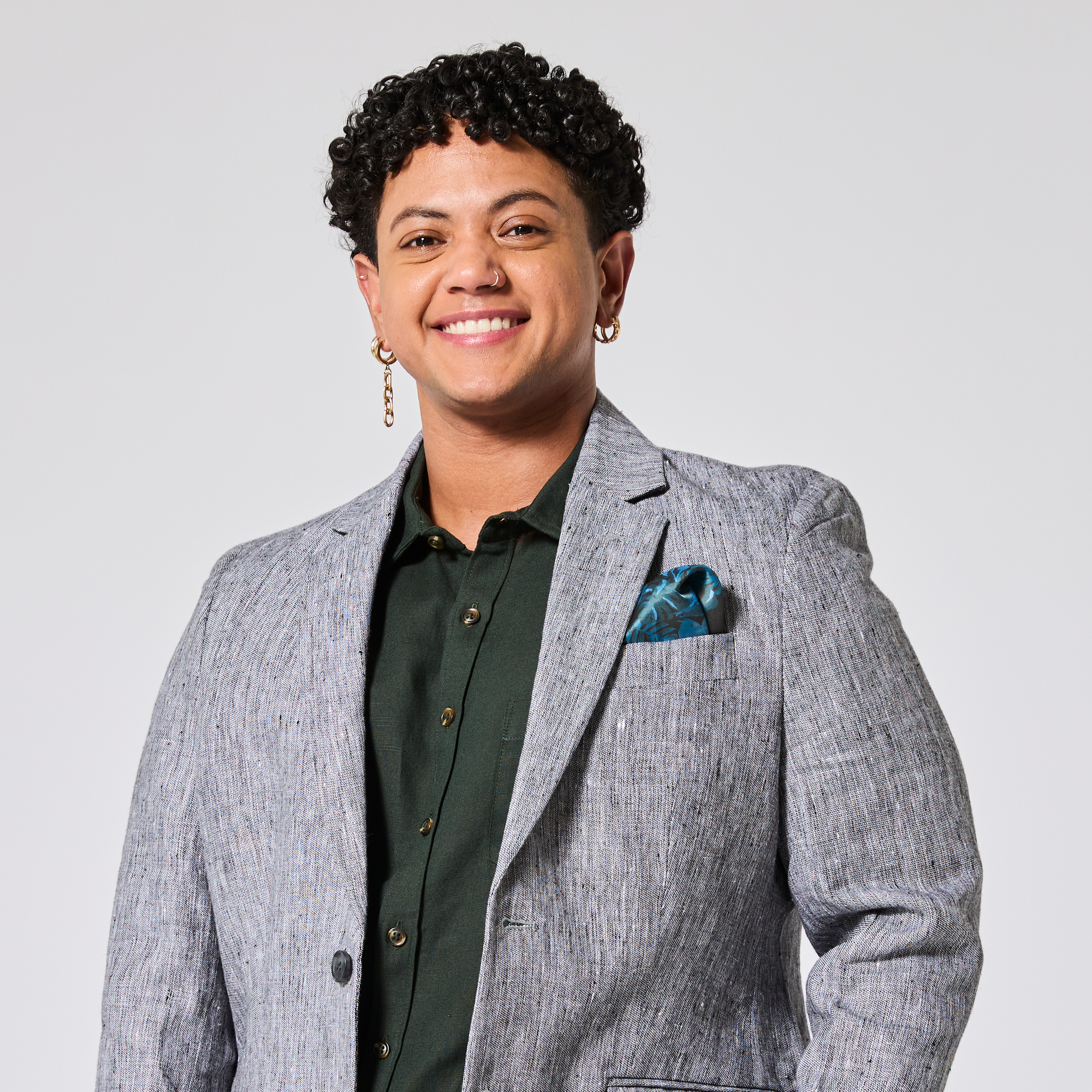 Person wearing a gray blazer with a green shirt and blue pocket square on a light gray background. Color: Graphite
