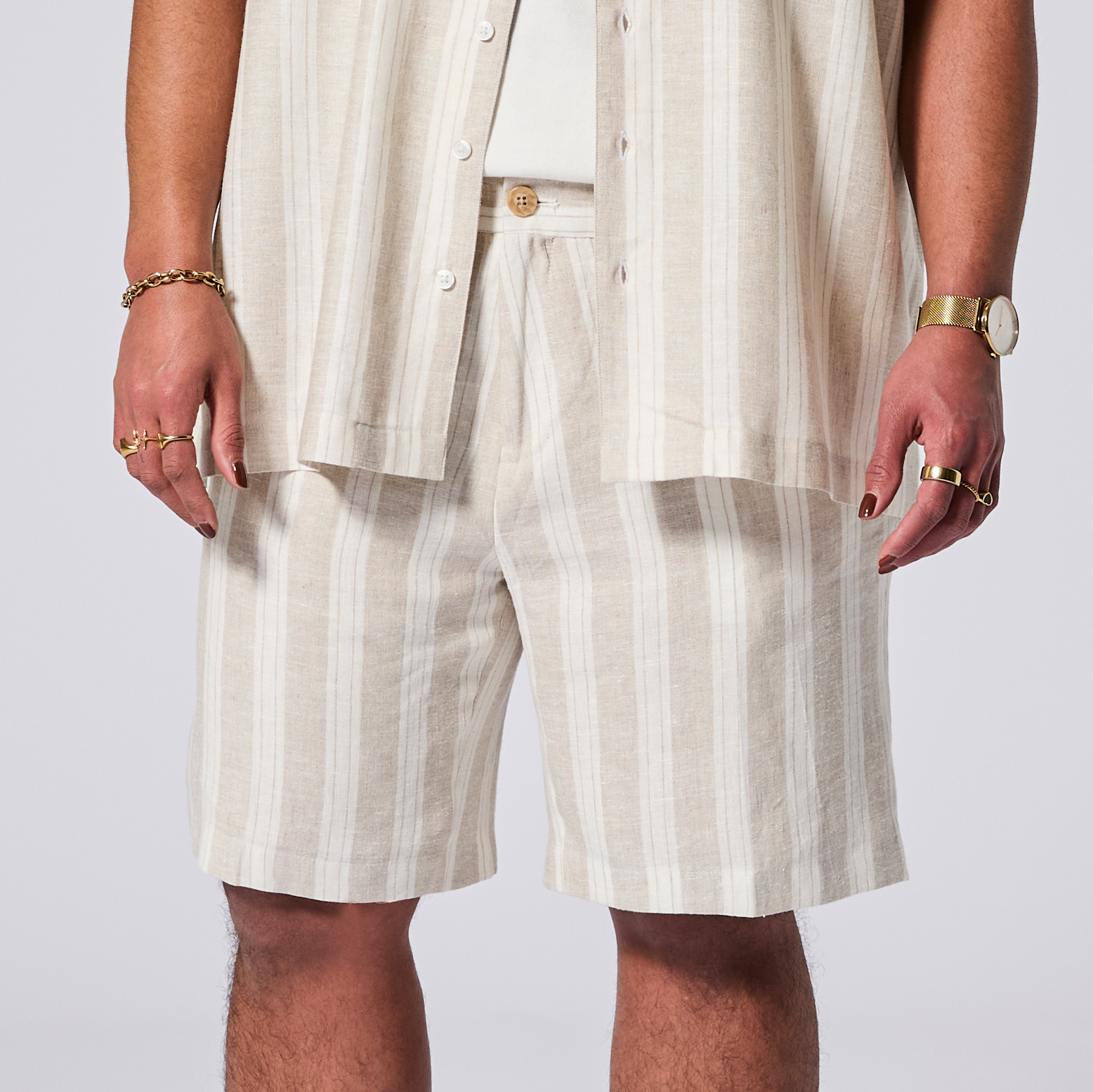 Person wearing beige striped shorts and a matching shirt on a white . background. Color: Sand Wide Stripe