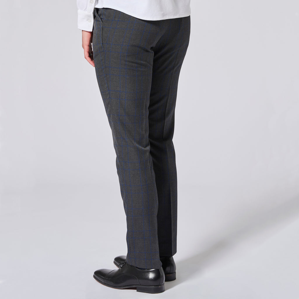 A person shown from the waist down wearing dark charcoal gray plaid trousers with a subtle blue windowpane pattern, paired with a white shirt and black leather dress shoes, against a light gray studio background. Color: Gray Admiral Plaid