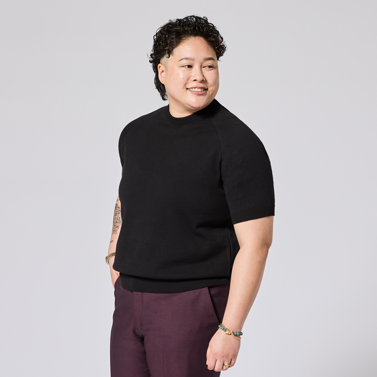 Model wearing a black knit shirt and purple pants on a light gray background. Color: Black