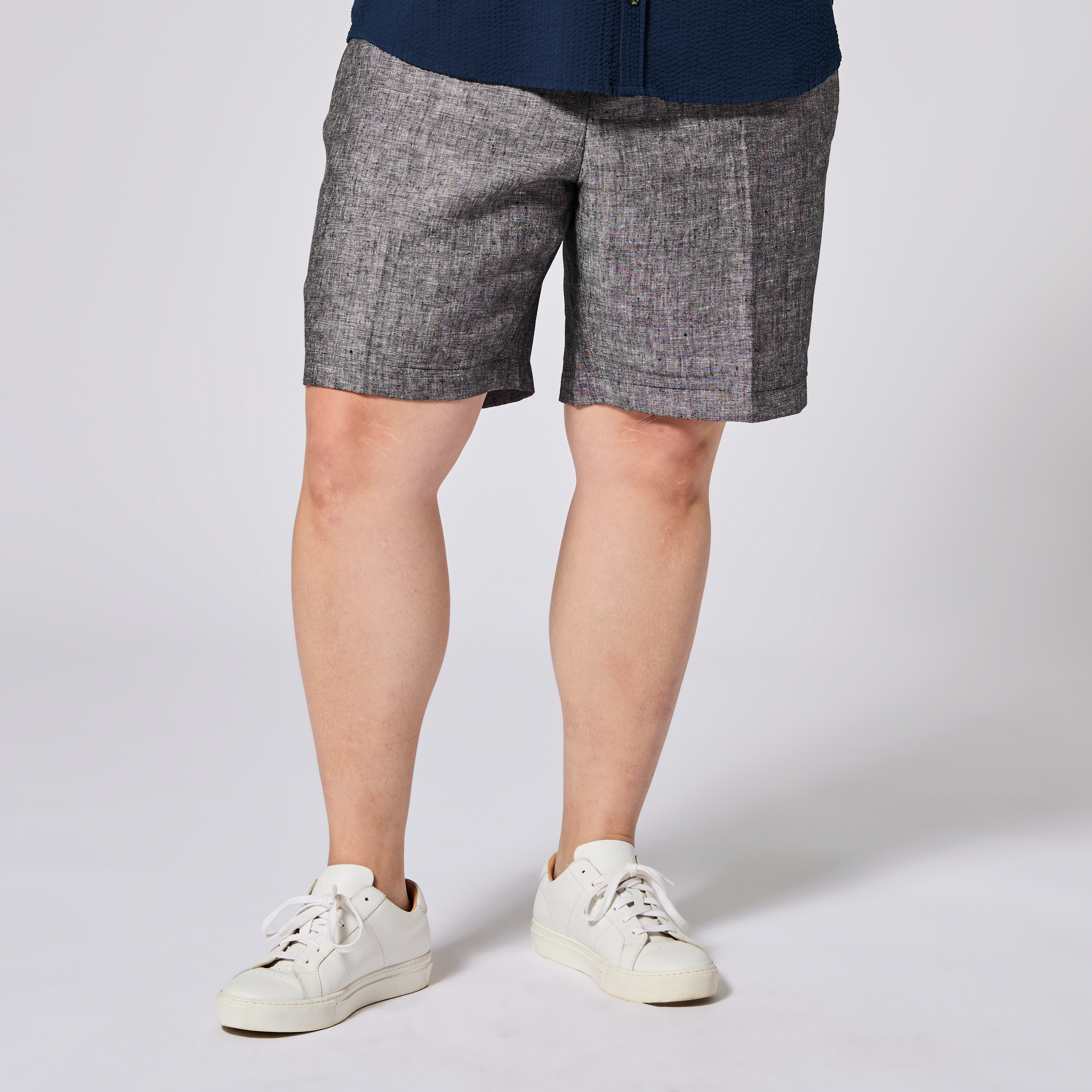 Person wearing gray shorts and white sneakers on a plain background. Color: Ash Gray