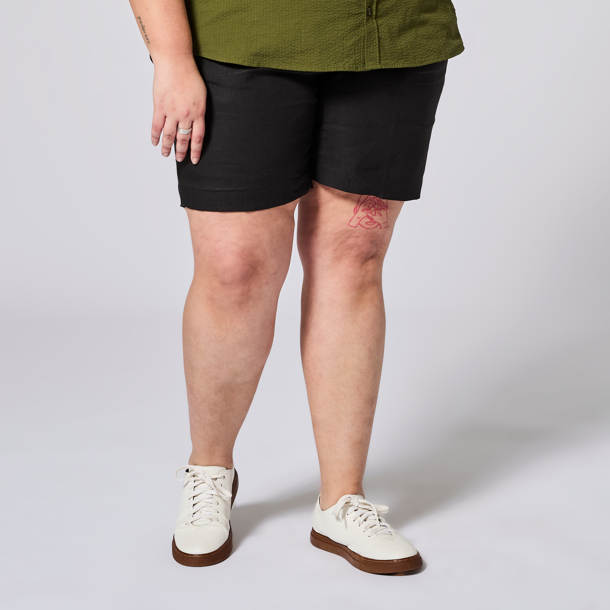 Person wearing black shorts and white sneakers on a plain background. Color: Black