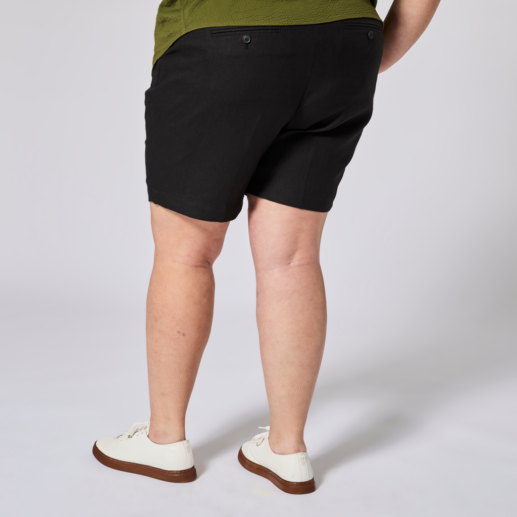 Person wearing black shorts and white sneakers on a plain background. Color: Black