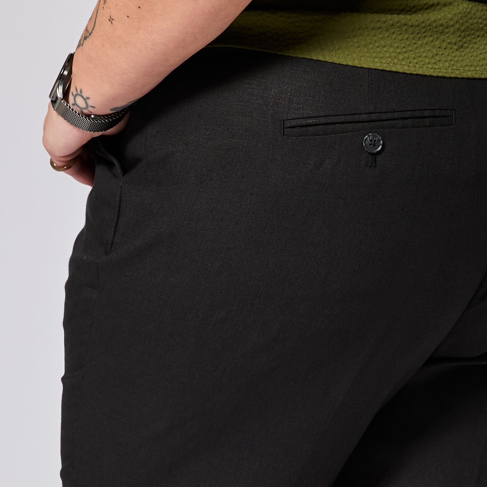 Close-up of black pants with a person's arm and green shirt in the background. Color: Black