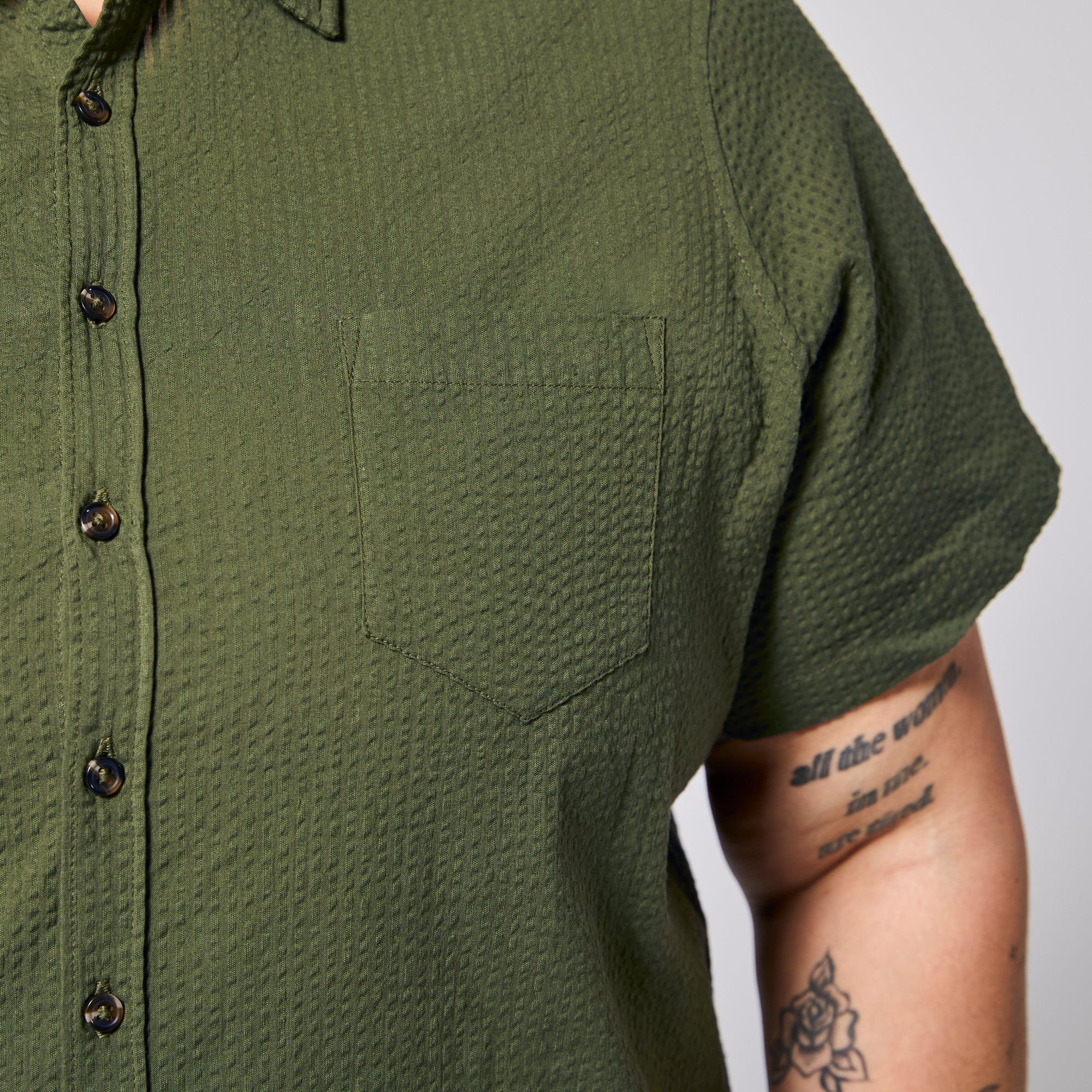Close-up of androgynous model wearing a green textured shirt with front pocket.  Color: Nopales