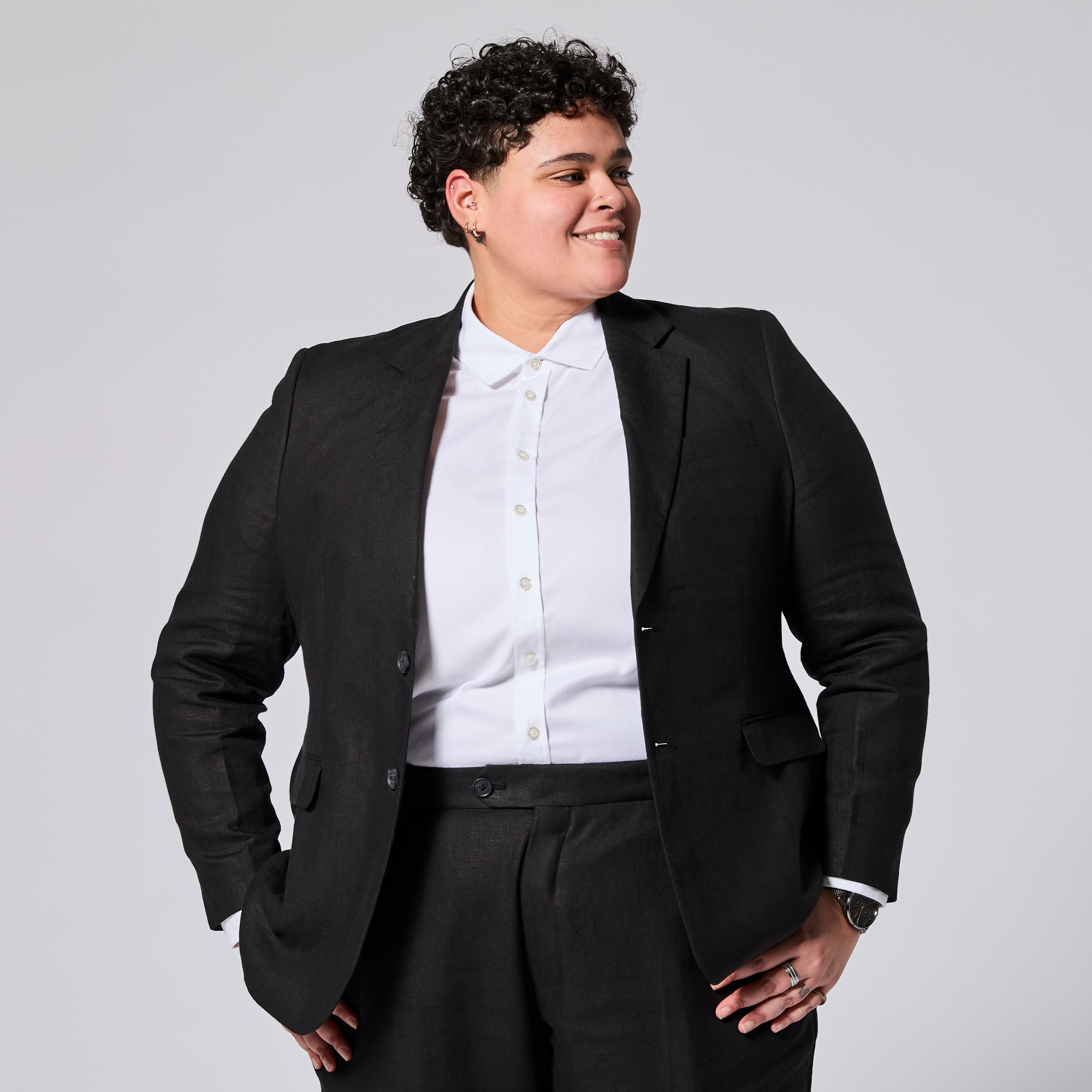 Person wearing a black suit jacket over a white shirt on a plain background. Color: Black