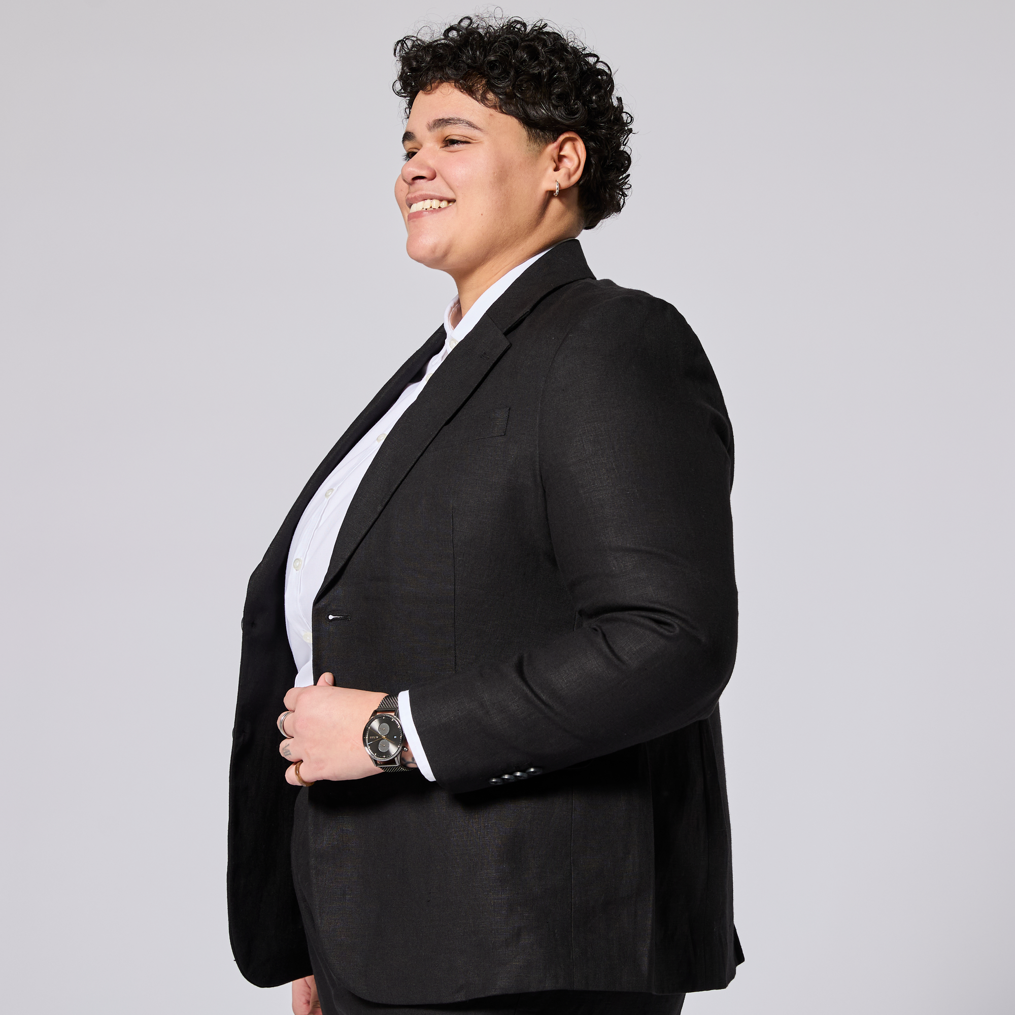 Person wearing a black suit jacket on a plain background. Color: Black