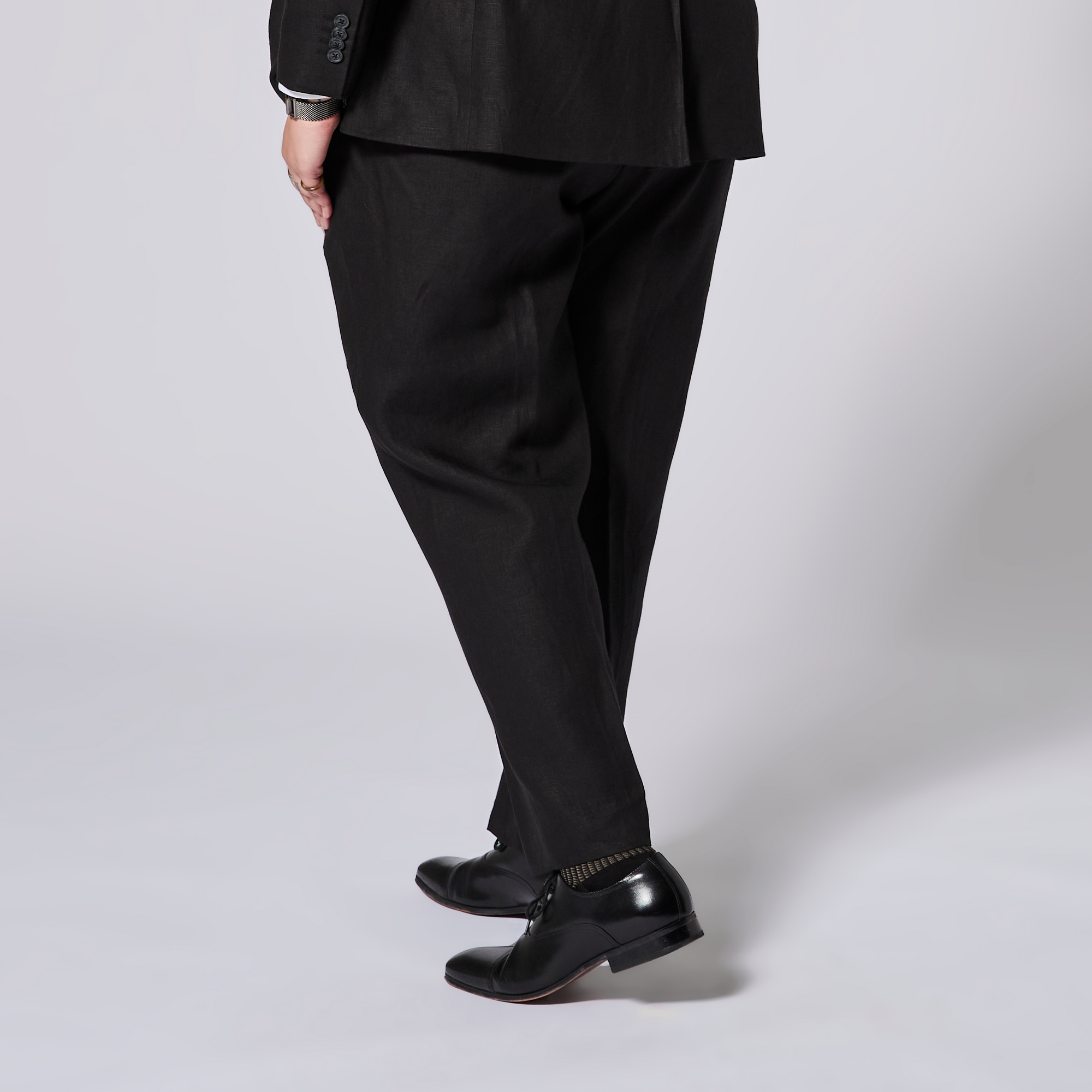 Person wearing a black suit and shoes on a light gray background. Color: Black