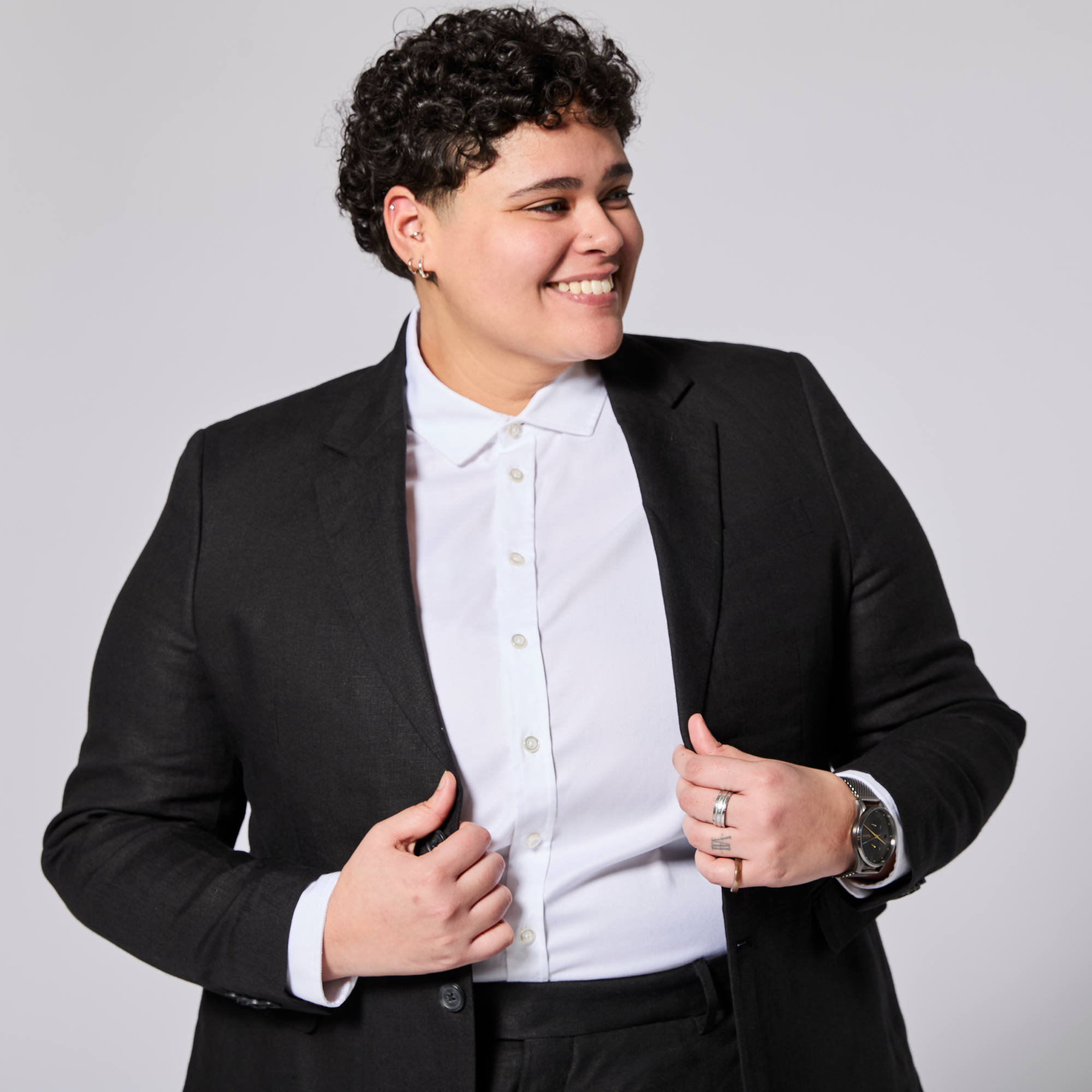 Person wearing a black blazer over a white shirt on a plain background. Color: Black