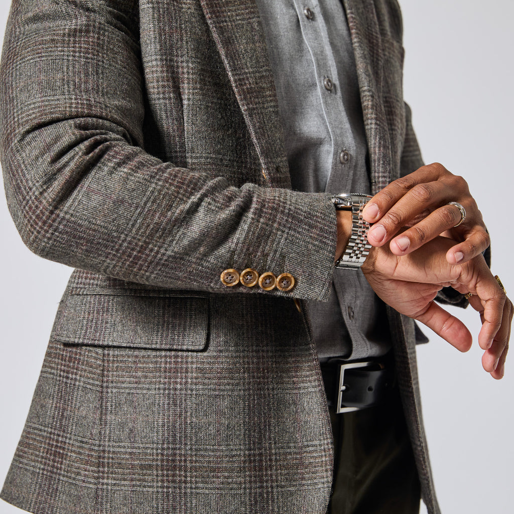 A close-up of a person wearing a gray and brown plaid blazer over a gray button-up shirt, with a silver metal link watch visible on the wrist. Color: Earthen Glen Plaid