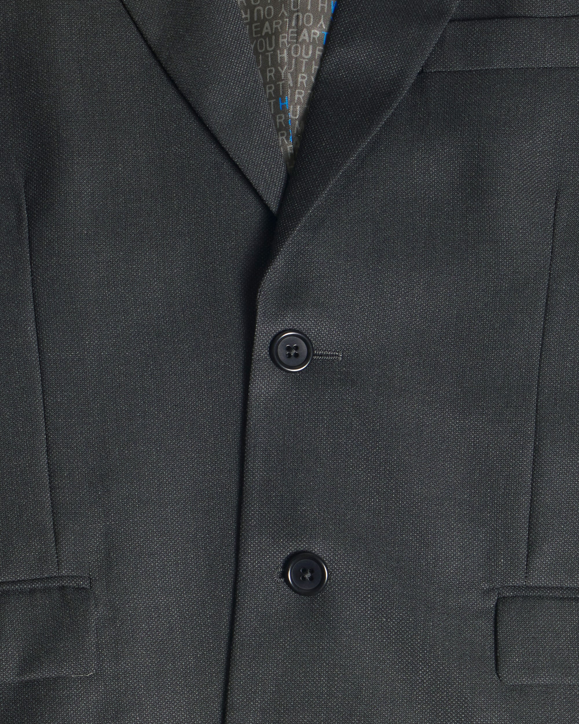 Close-up of a dark charcoal gray suit jacket with two buttons, showing the fine twill texture of the fabric and a patterned inner collar lining. Color: Nightfall Birdseye