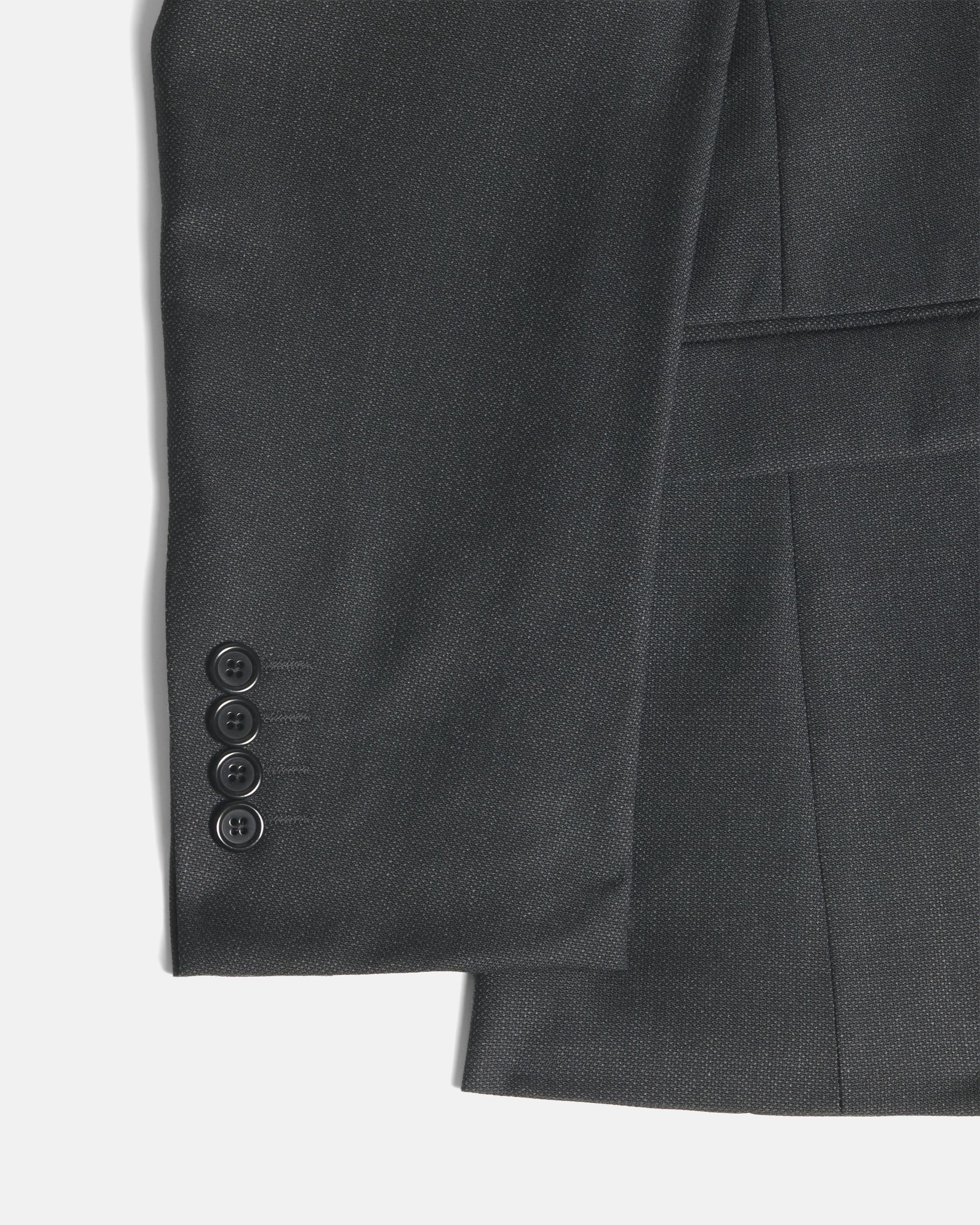 Close-up of a dark charcoal gray suit jacket showing the sleeve with four buttons and a pocket detail against a light gray background. Color: Nightfall Birdseye