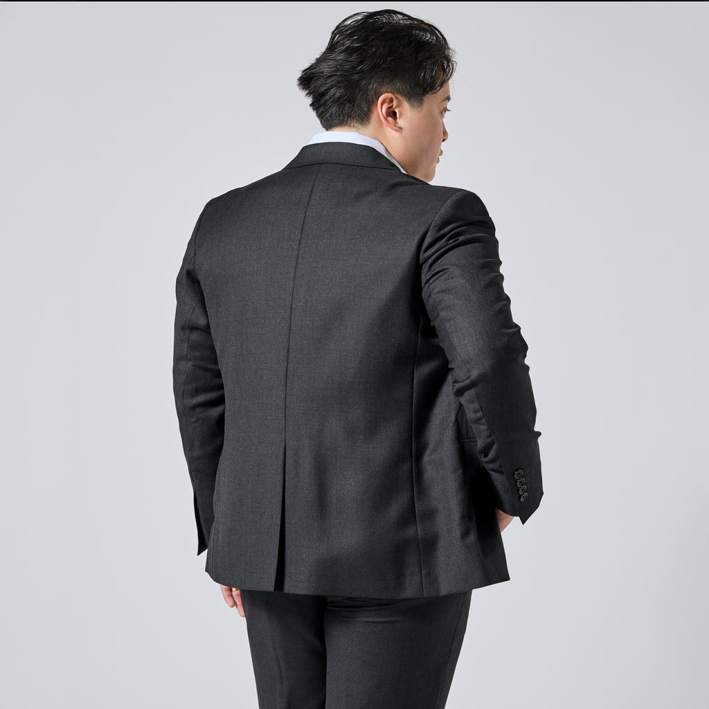 Person wearing a dark charcoal gray suit jacket, shown from the back and three-quarter side view against a light gray studio background. Color: Nightfall Birdseye