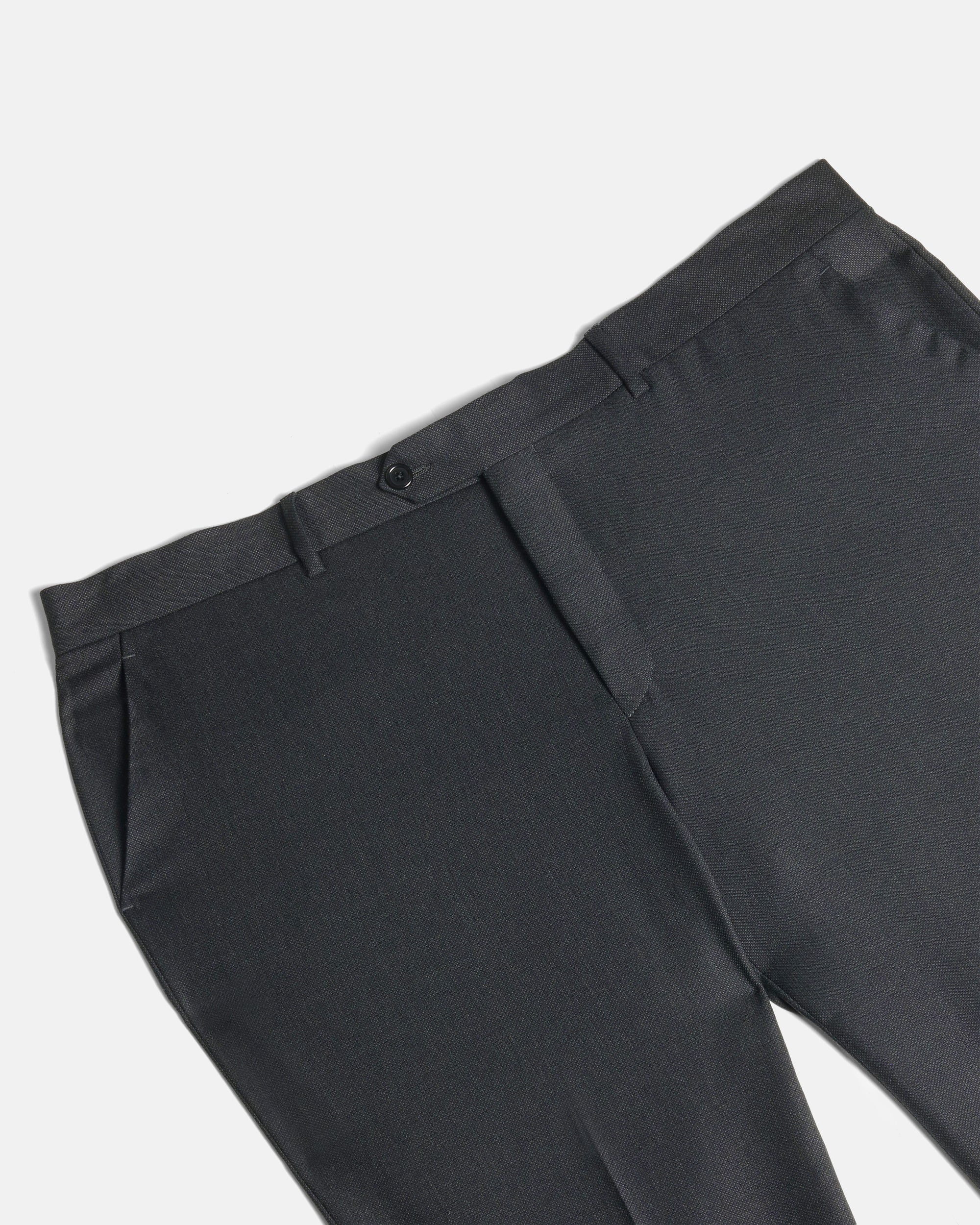 Close-up of dark charcoal gray tailored trousers showing the waistband, belt loops, button, front fly, and side pocket on a light gray background. Color: Nightfall Birdseye