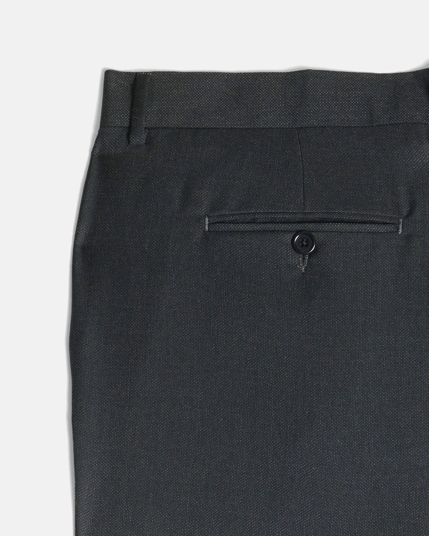 Close-up of the back waistband and rear pocket of dark charcoal gray trousers, showing a single button closure and fabric texture against a light gray background. Color: Nightfall Birdseye