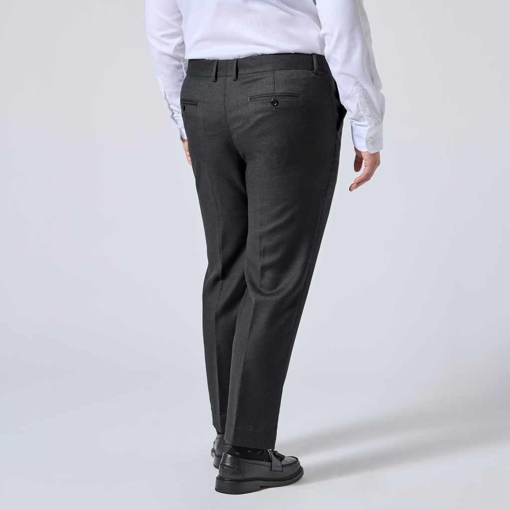 A person shown from the back wearing dark charcoal gray dress pants, a white long-sleeve shirt, and black loafers against a light gray studio background. Color: Nightfall Birdseye