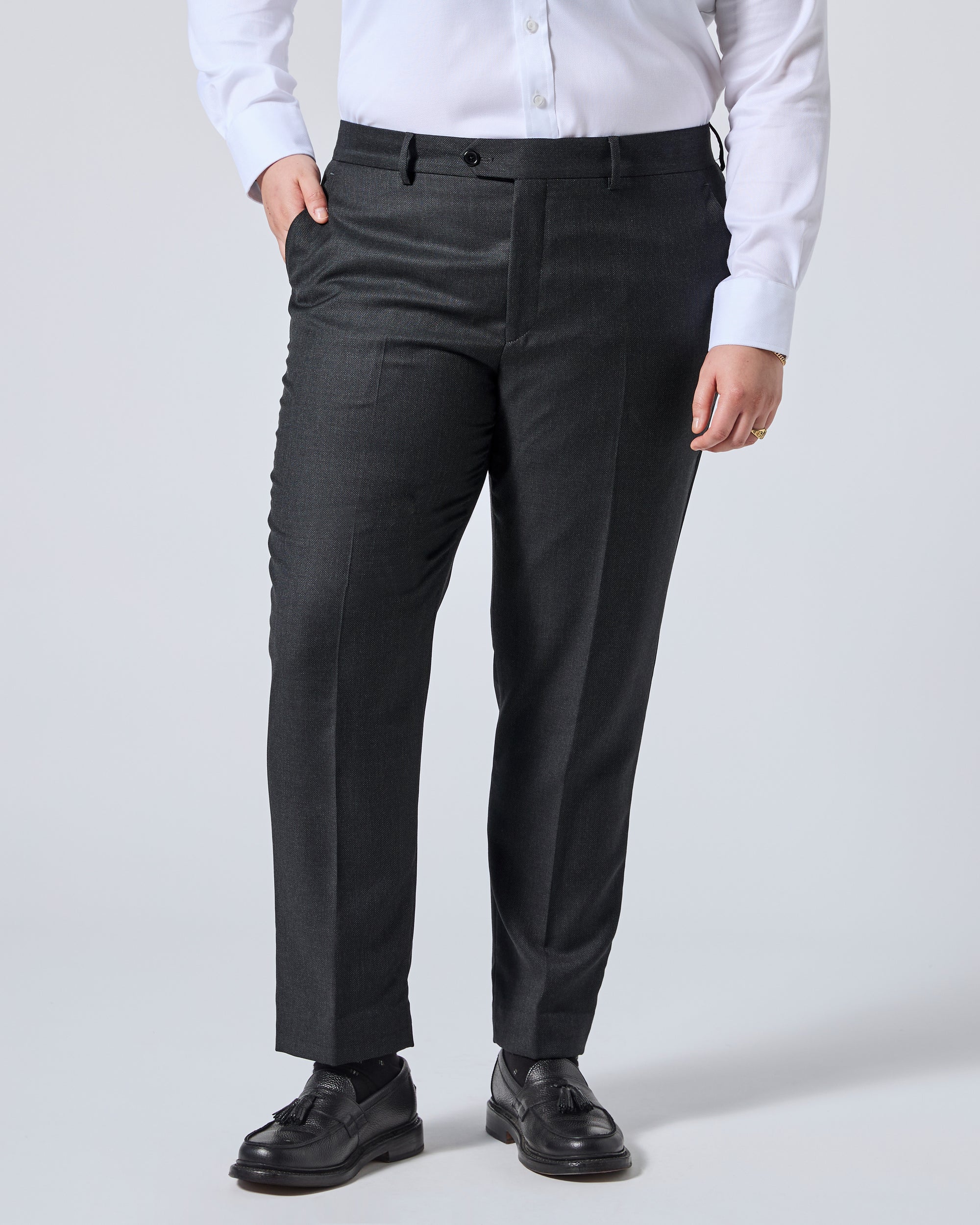 A person wearing dark charcoal gray dress pants with a white button-down shirt and black leather shoes, shown from the waist down against a light gray studio background. Color: Nightfall Birdseye