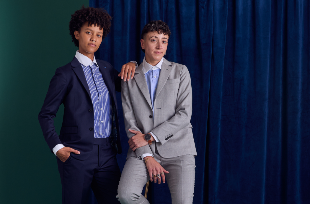 Two people in suits standing against a blue curtain