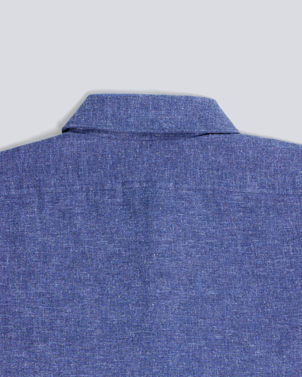 Close-up of the back collar and upper back of a textured blue shirt on a light gray background. Color: Blue Marl