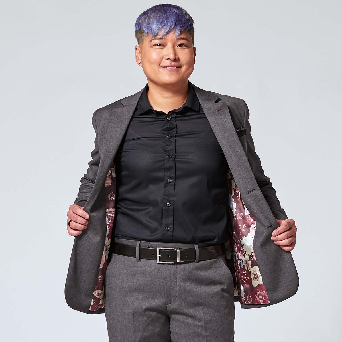 Person wearing a gray blazer with floral interior, black shirt, and gray pants on a light gray background