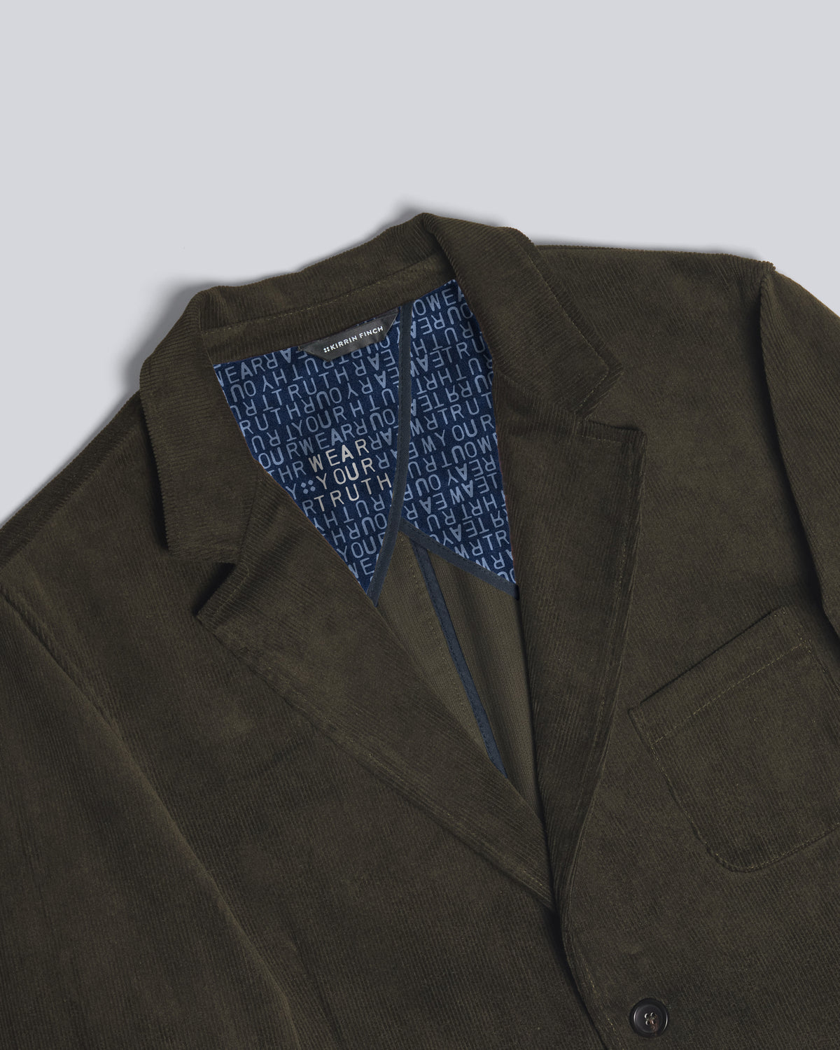 Close-up of an olive green blazer jacket with a blue patterned lining visible inside the collar, set against a light gray background. Color: Pine