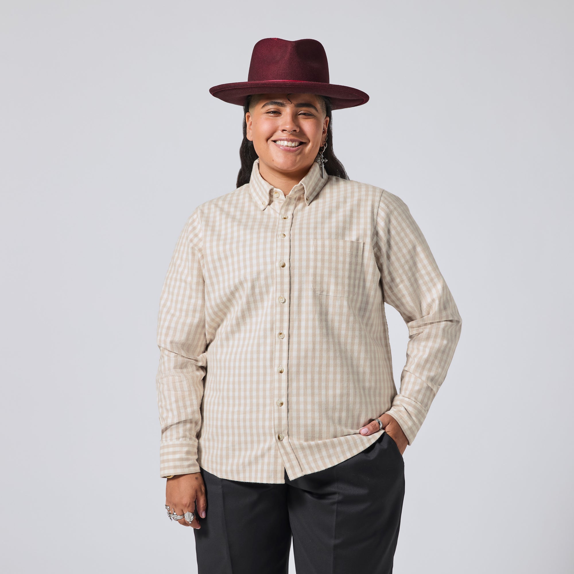 Model in a beige and white gingham long-sleeve button-down shirt, paired with dark gray pants and a burgundy wide-brim hat, against a solid light gray background. Color: Cream Check