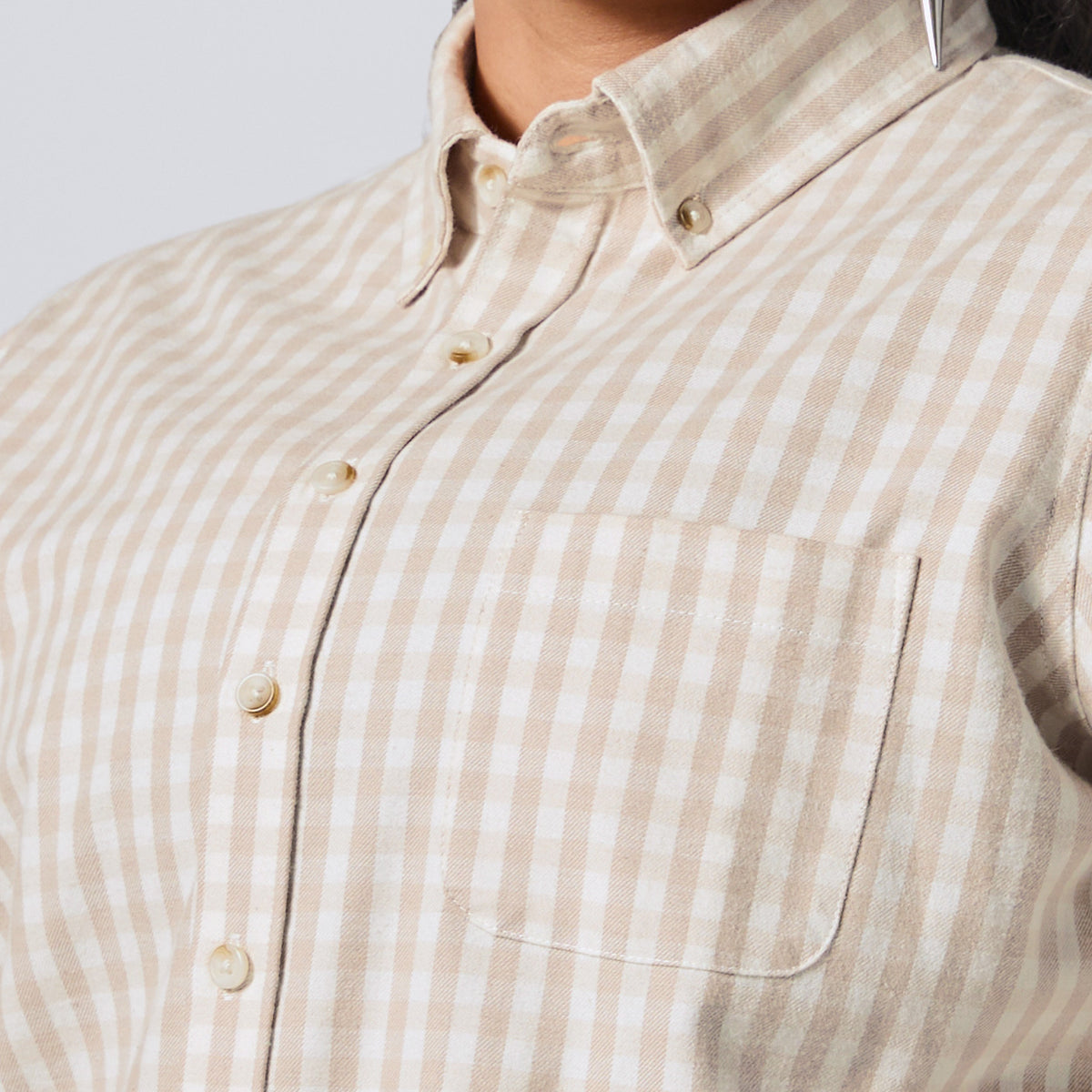 Close-up of a person wearing a beige and white gingham button-down shirt with a chest pocket, showing the collar, buttons, and fabric texture. Color: Cream Check