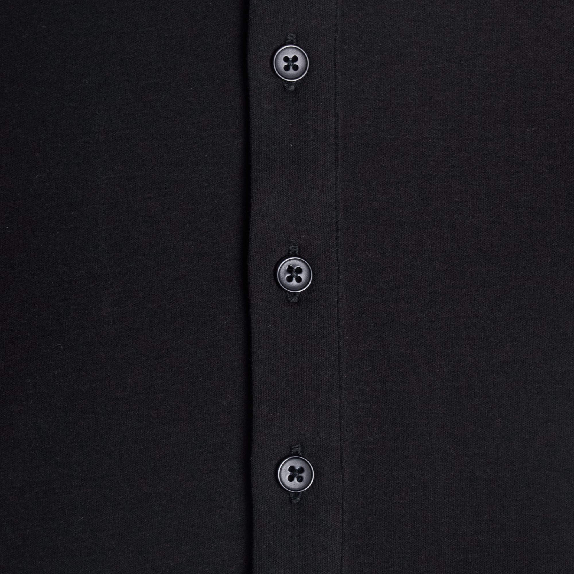 Close-up of a black shirt with buttons on a plain background. Color: Black