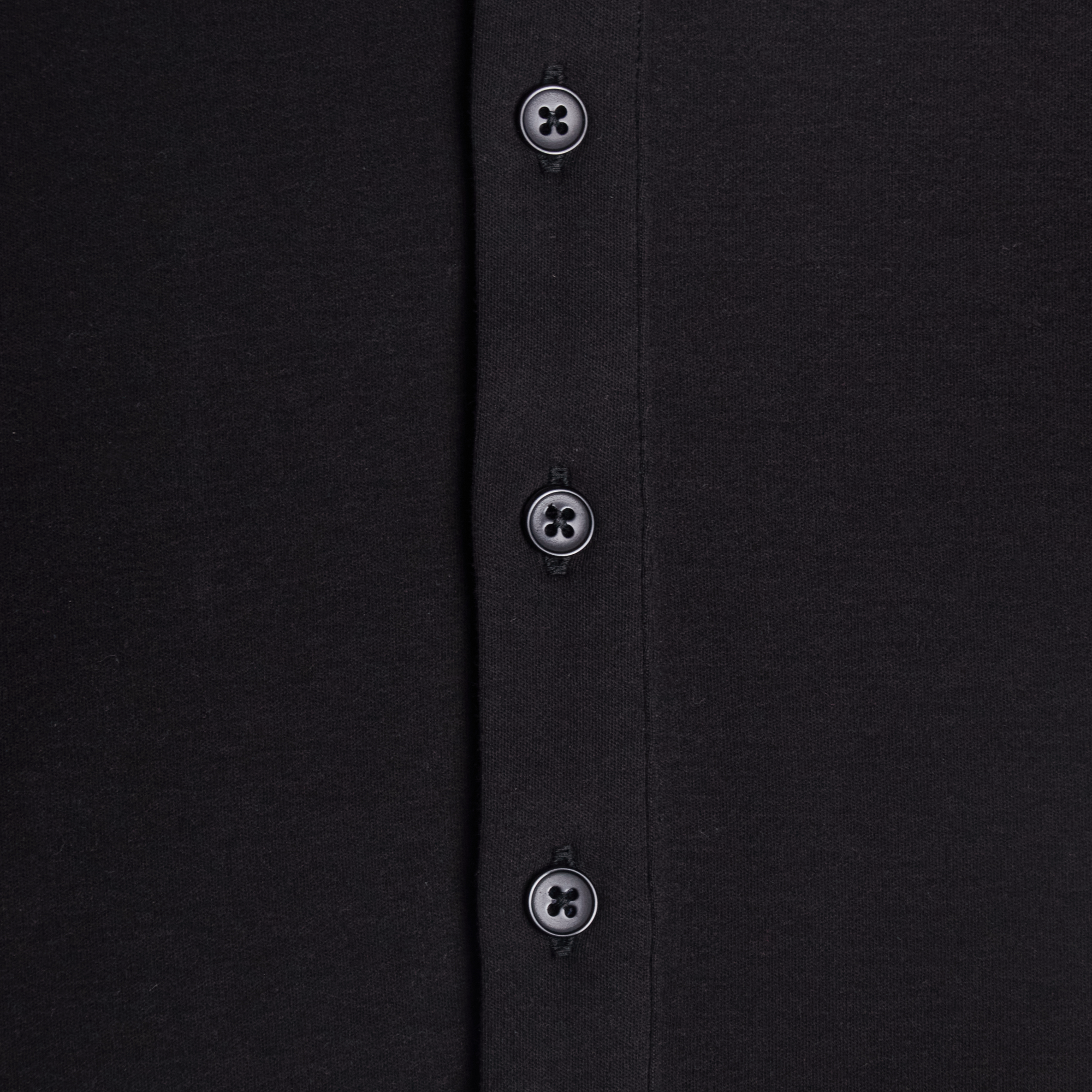 Close-up of a black shirt with buttons on a plain background. Color: Black