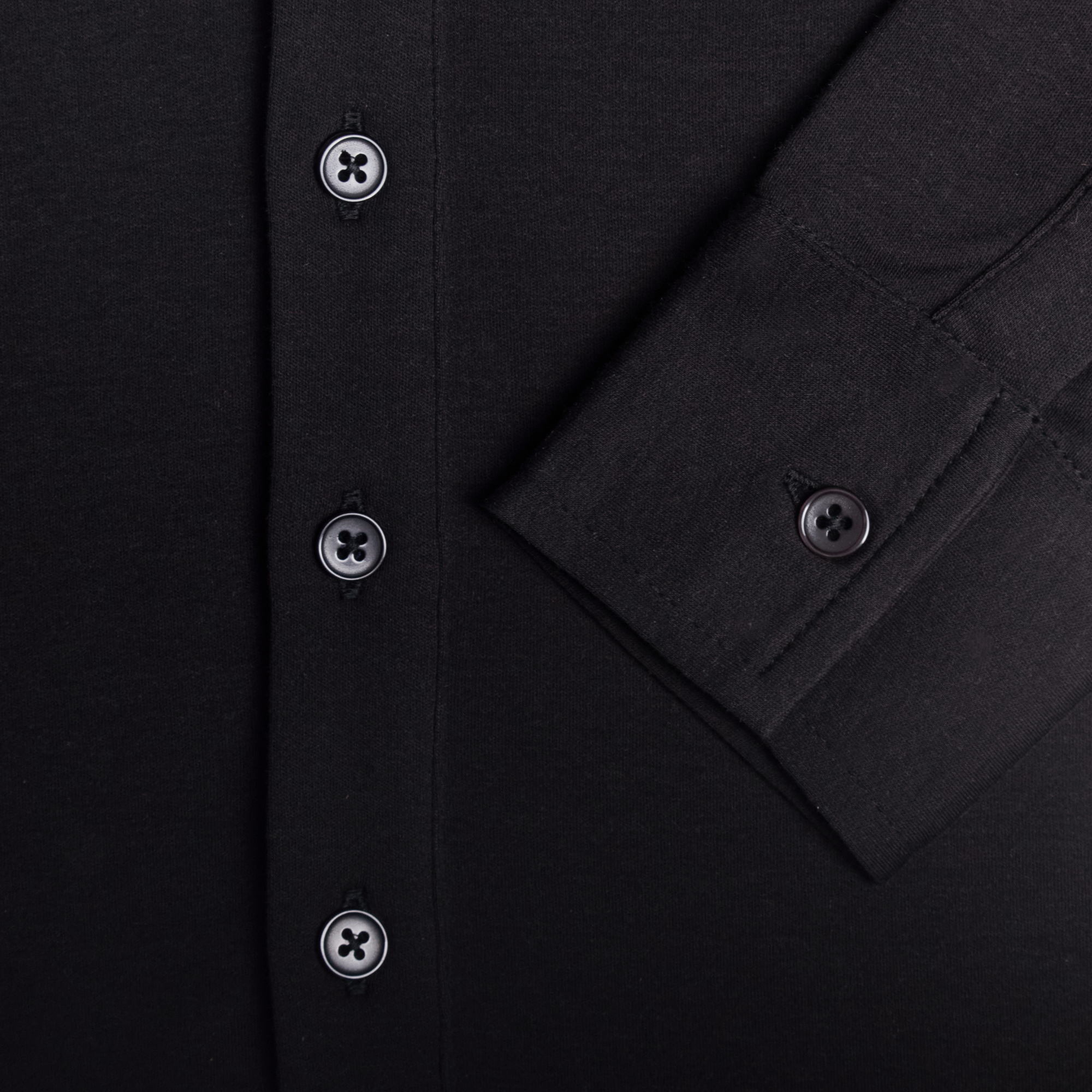 Close-up of a black shirt with button details. Color: Black