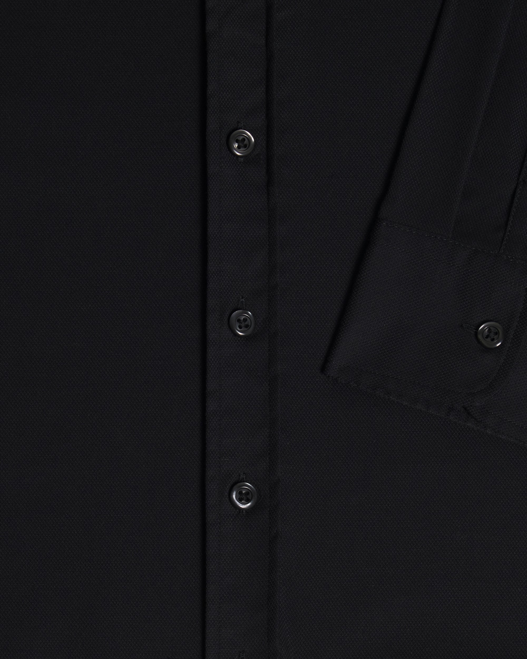 Close-up of a black button-up shirt showing the front button placket, fabric texture, and sleeve cuff details. Color: Black