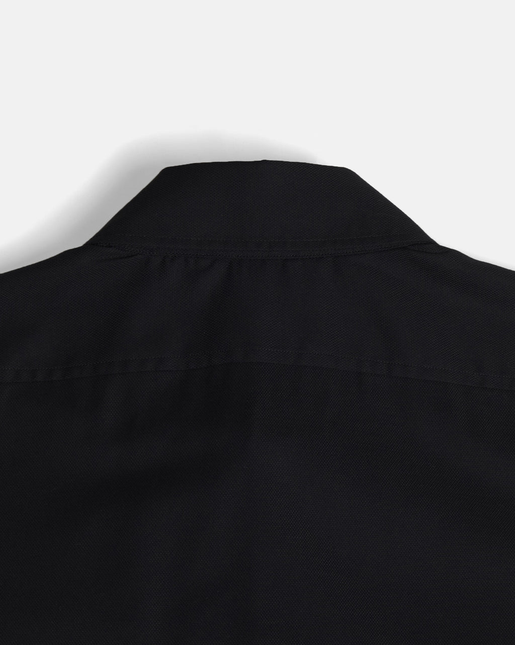 Close-up of the collar and shoulder area of a black button-down shirt taken from behind. Color: Black