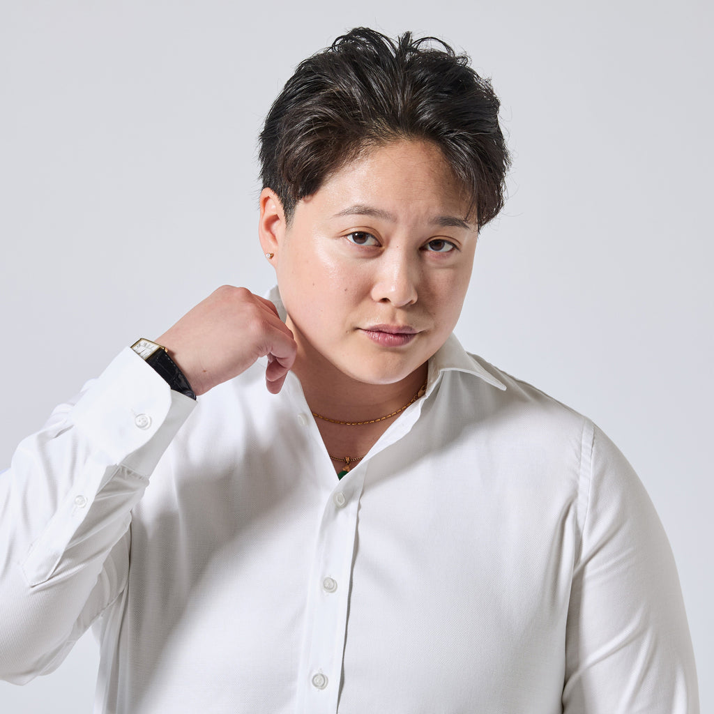 Model wearing a white long-sleeve button-up shirt, standing against a light gray background with one hand by their neck. Color: White